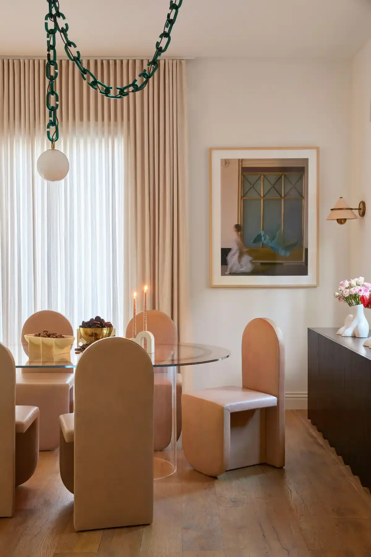 Warm contemporary dining space with camel leather chairs, glass table, green chain pendant and soft drapery light.
