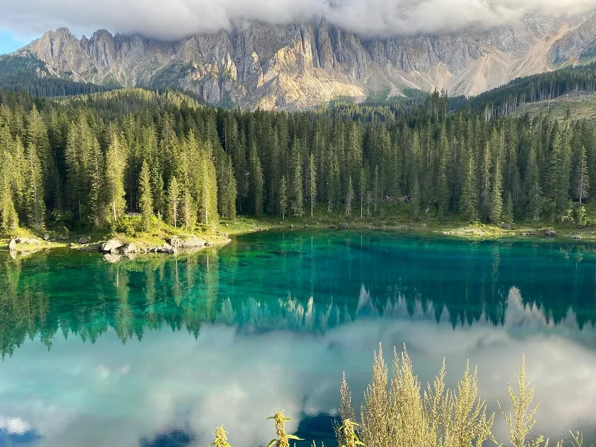  Lago di Carezza in the Dolomites with turquoise water reflecting pine forest and jagged peaks. 