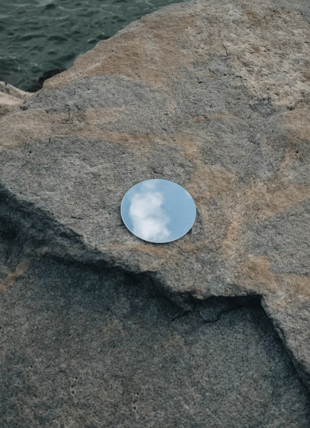 Small circular mirror placed on a textured stone surface.