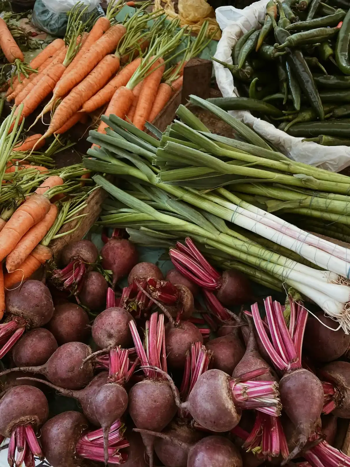 Colorful farmers’ market display of carrots, beets and scallions piled high on wooden crates.