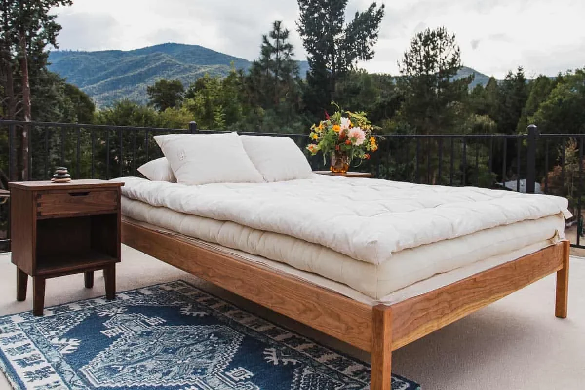 Shepherd’s Dream Snuggle-Mate wool topper on an outdoor bed overlooking forested mountains.
