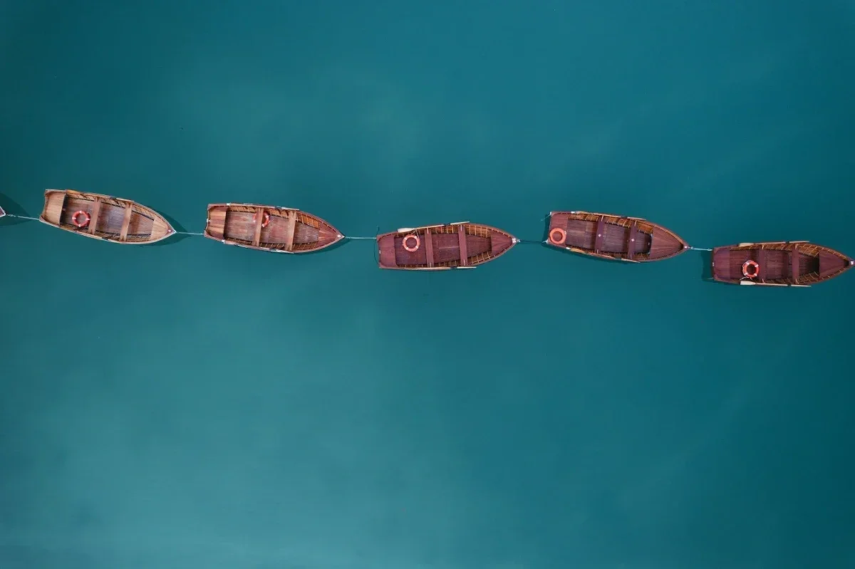  Wooden rowboats aligned on turquoise alpine lake in the Dolomites from aerial view. 