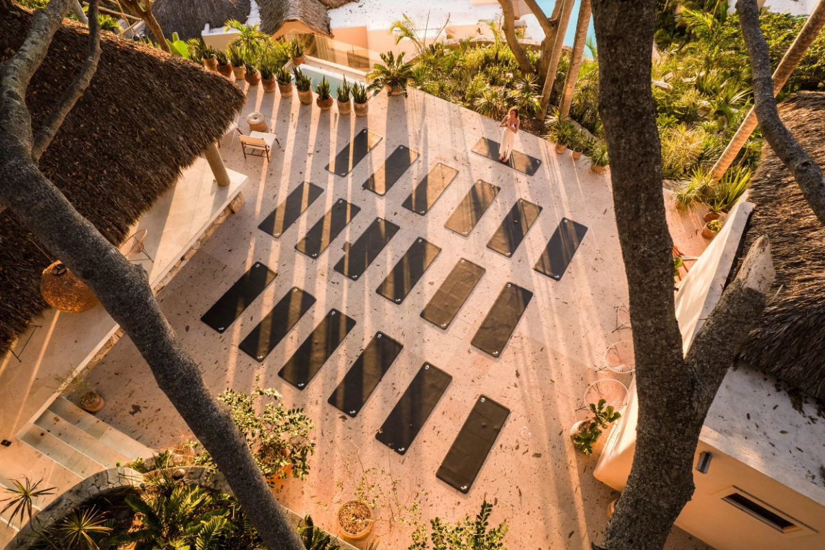 Sunlit terrace lined with neat rows of yoga mats between palapa roofs and jungle at La Joya Sayulita retreat.