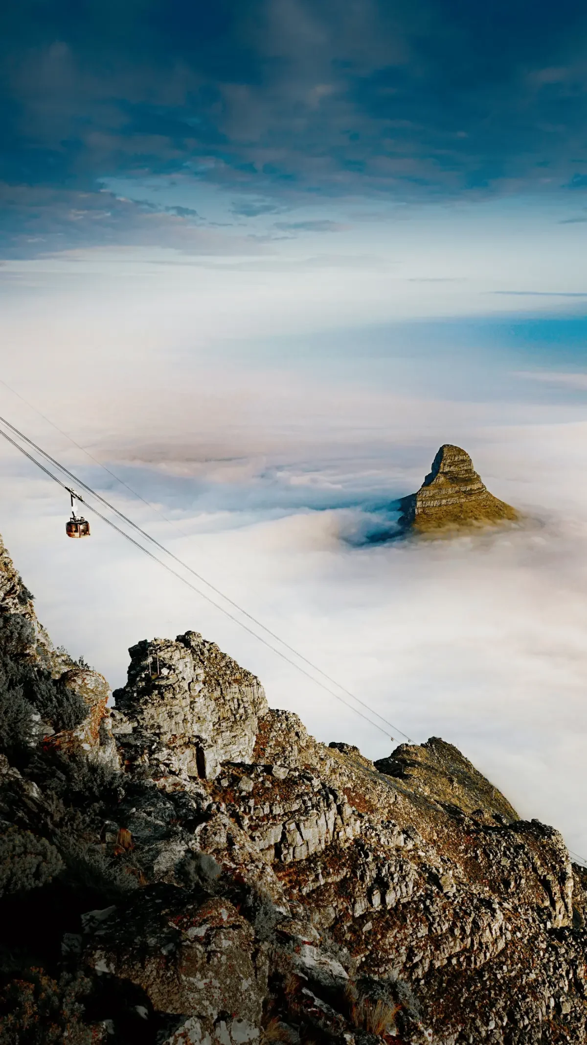 Cable car glides up Table Mountain above a cloud inversion with Lion’s Head poking through the morning mist.