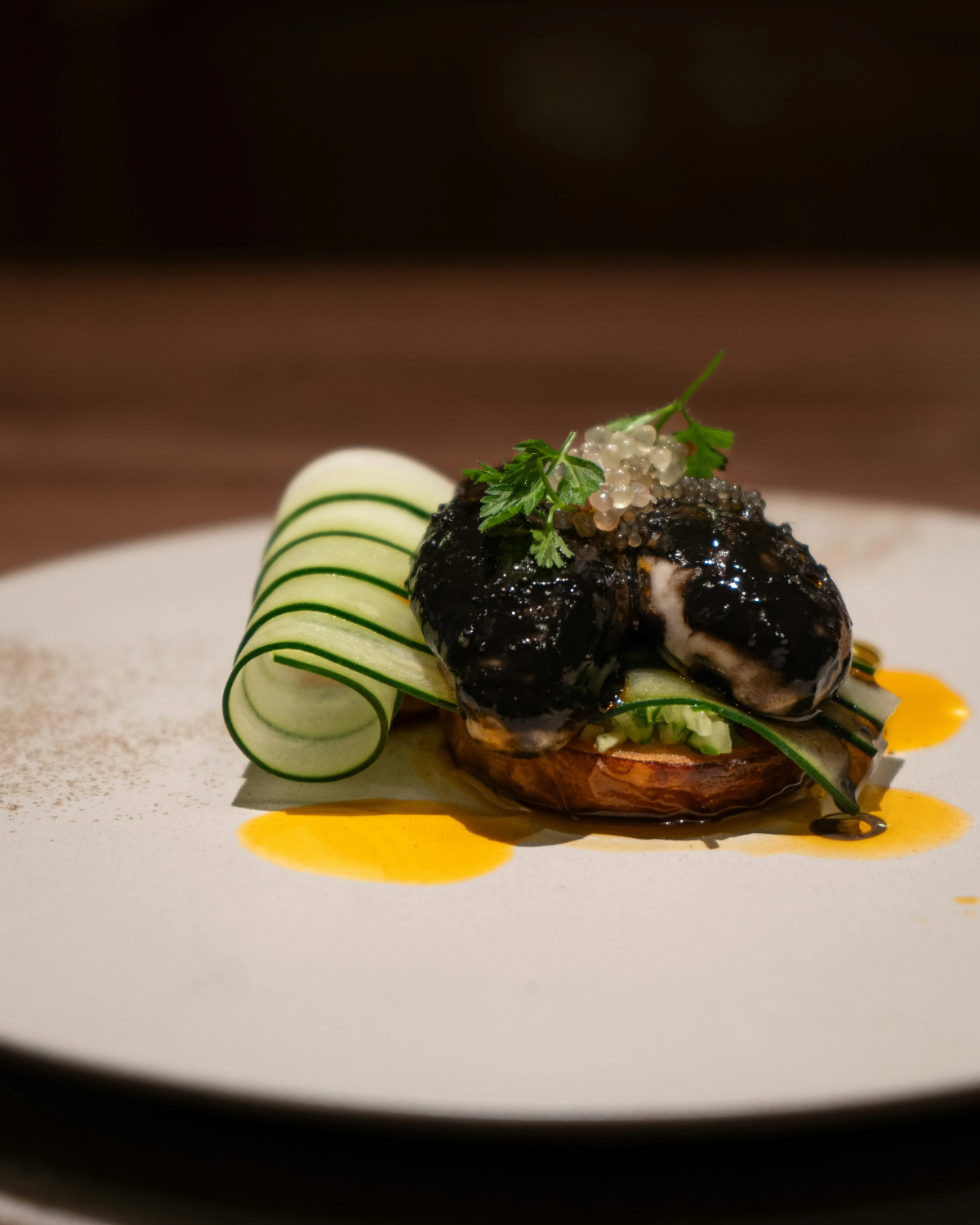 Michelin-level plated dish of squid-ink croquette topped with caviar, curled cucumber ribbon and saffron sauce.