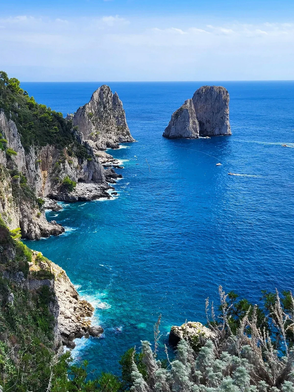 Dramatic Faraglioni sea stacks off Capri rise from bright-blue Tyrrhenian waters below rugged cliffs.