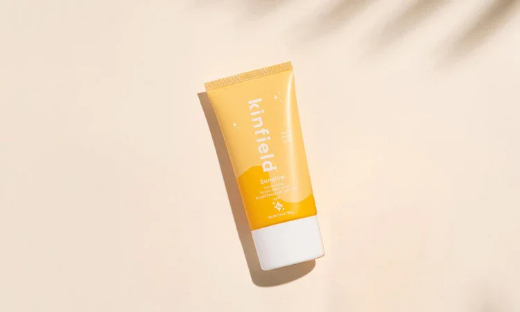 Soft-peach backdrop highlights Kinfield Sunglow SPF 30 illuminating sunscreen.