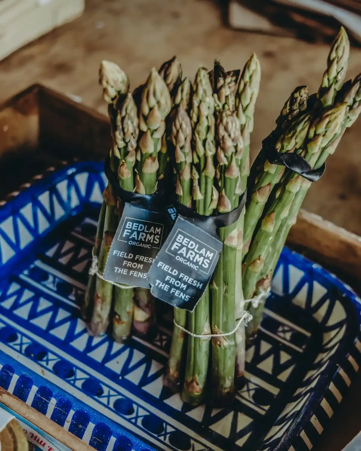 Bundles of organic asparagus labeled Bedlam Farms resting in a patterned tray.