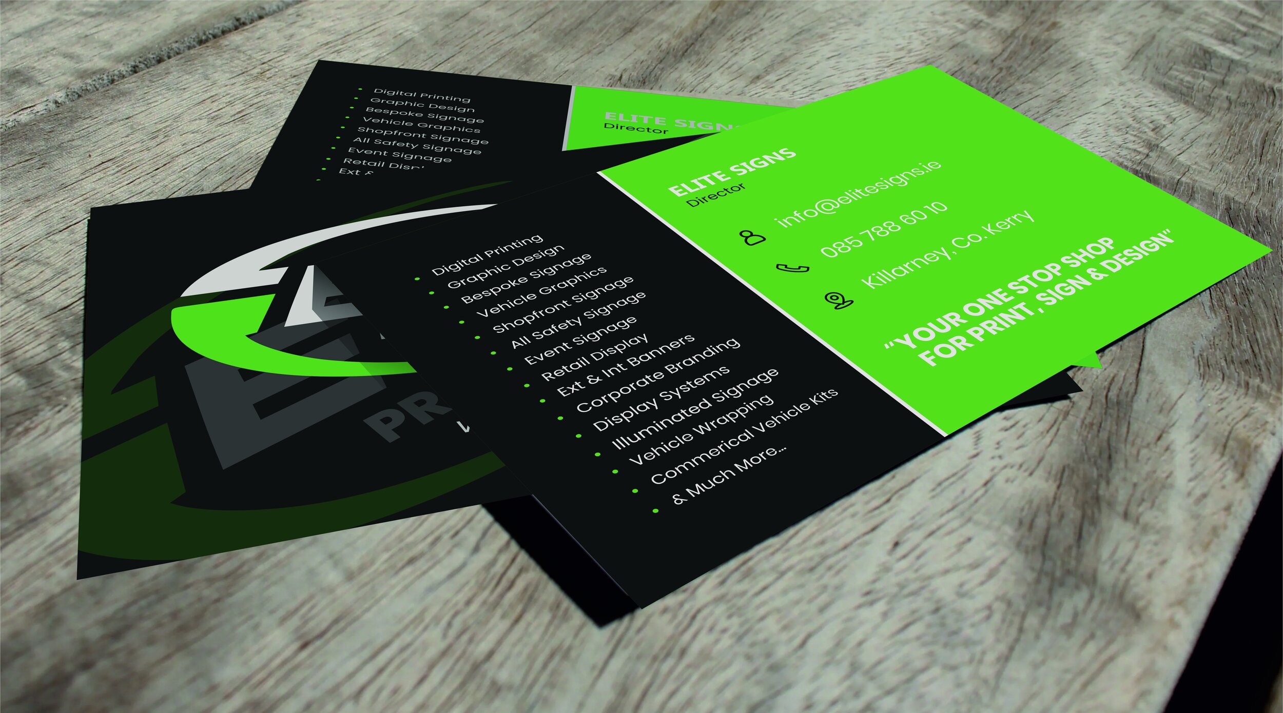 Stack of business cards with dark and neon green design, featuring company name, contact details, and services like digital printing, graphic design, and vehicle wrapping, placed on a wooden surface. Signmakers Cork & Kerry, Ireland.