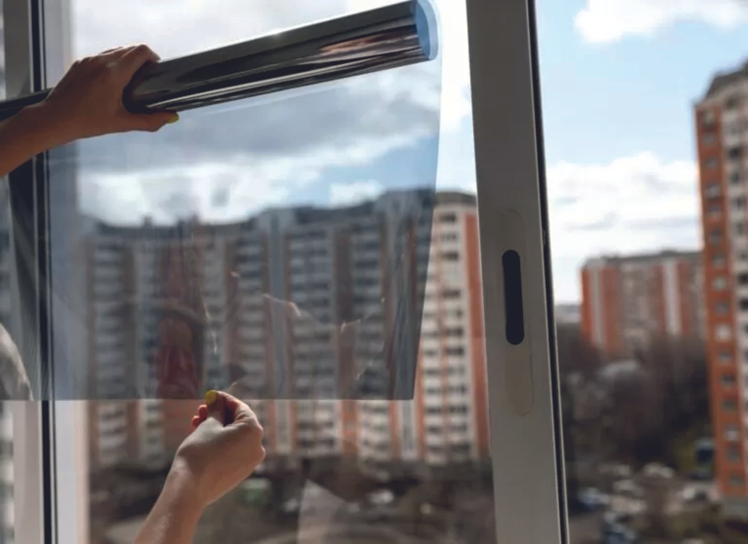 Person applying window film on glass with cityscape backdrop. Signmakers Cork & Kerry, Ireland.