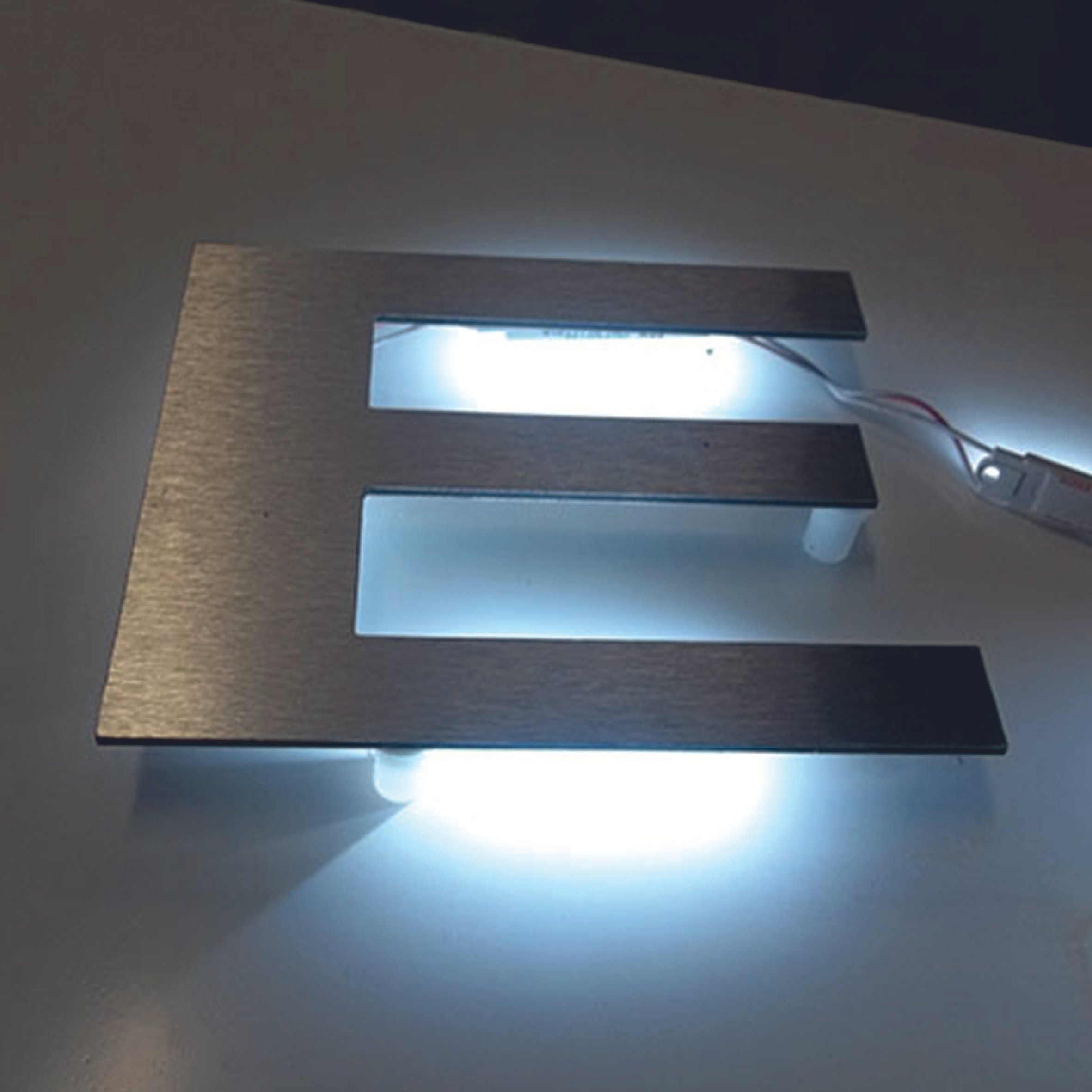 Illuminated brushed metal letter E with LED lights on a white surface. Raised LED Letters. Illuminated signage. Signmakers Cork & Kerry, Ireland.