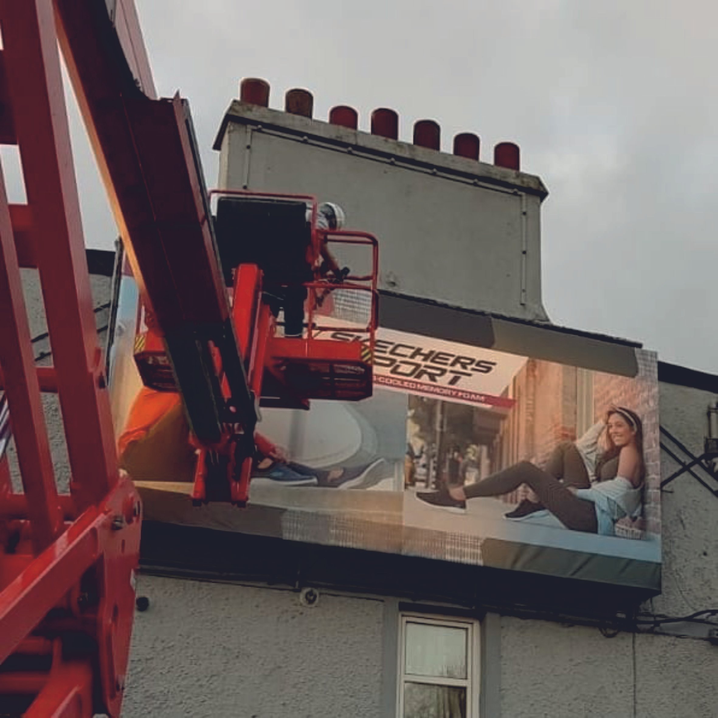 Person in a cherry picker installing a large banner advertisement on a building exterior. Signmakers Cork & Kerry, Ireland.