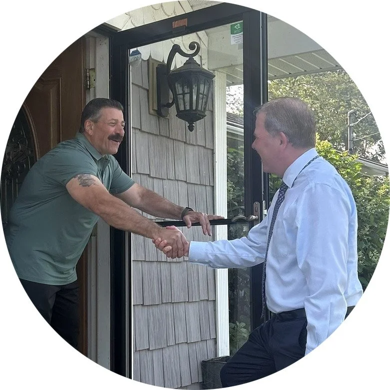 Larry Burke stands at a resident's doorstep as the homeowner reaches out and shakes his hand.
