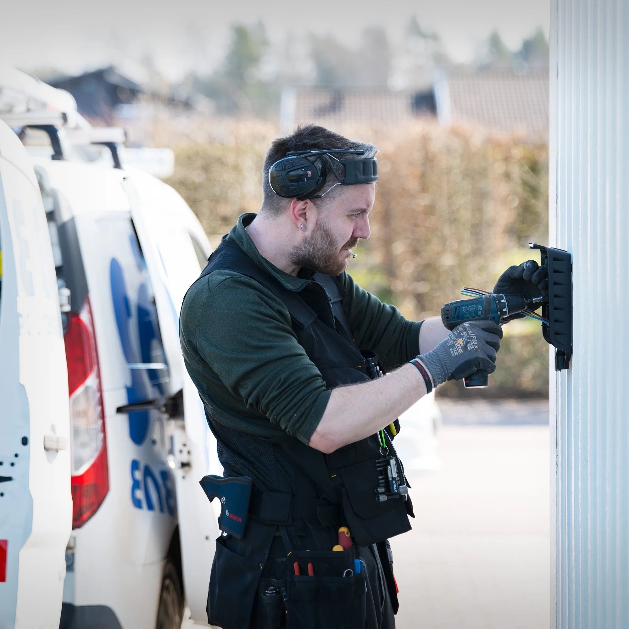 Man som använder felsökningsutrustning utomhus, med en vit bil i bakgrunden.