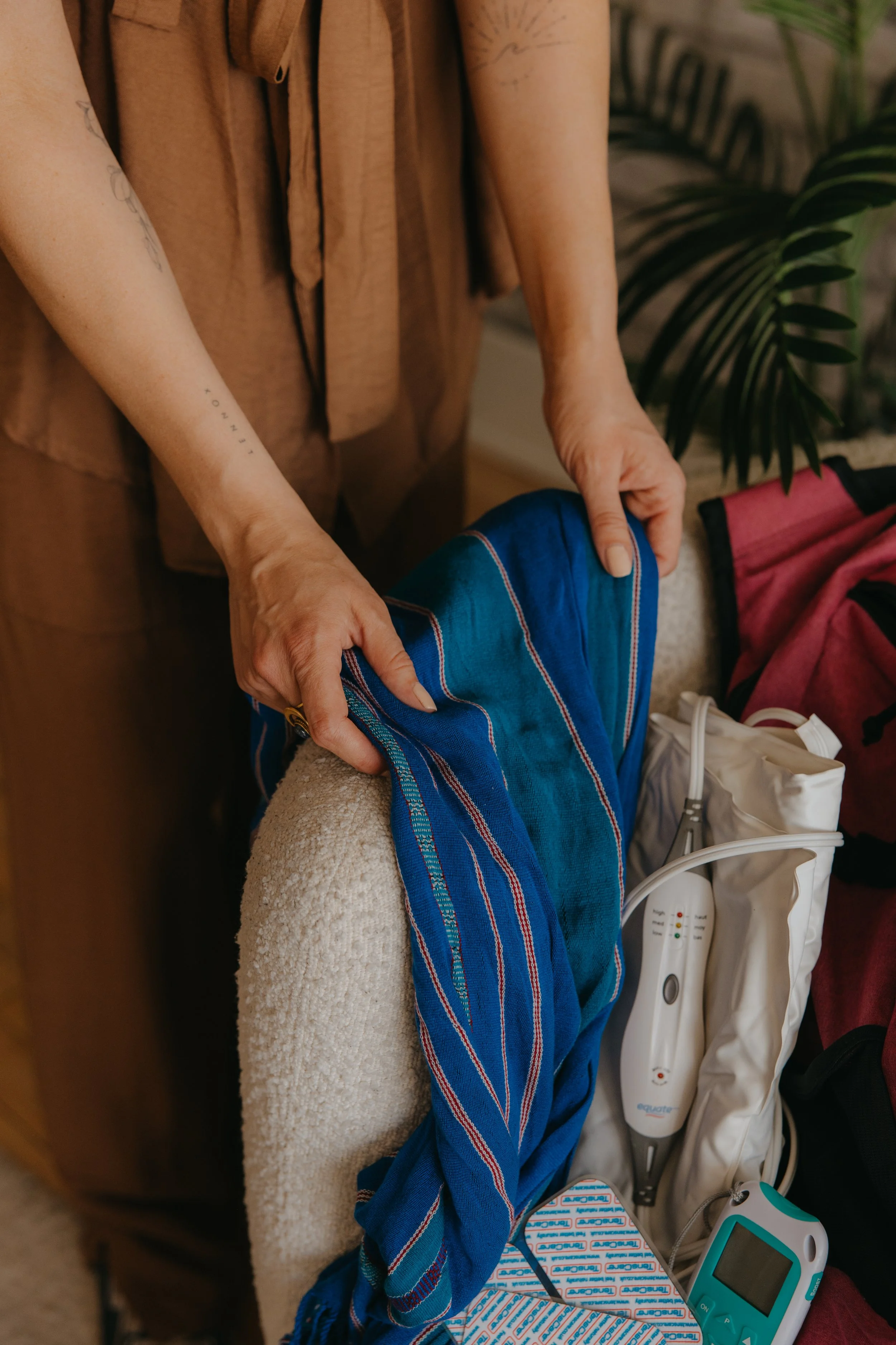 Person packing a blue striped rebozo into a doula's birth bag. A TENS machine, heating pad, and backpack are visible.
