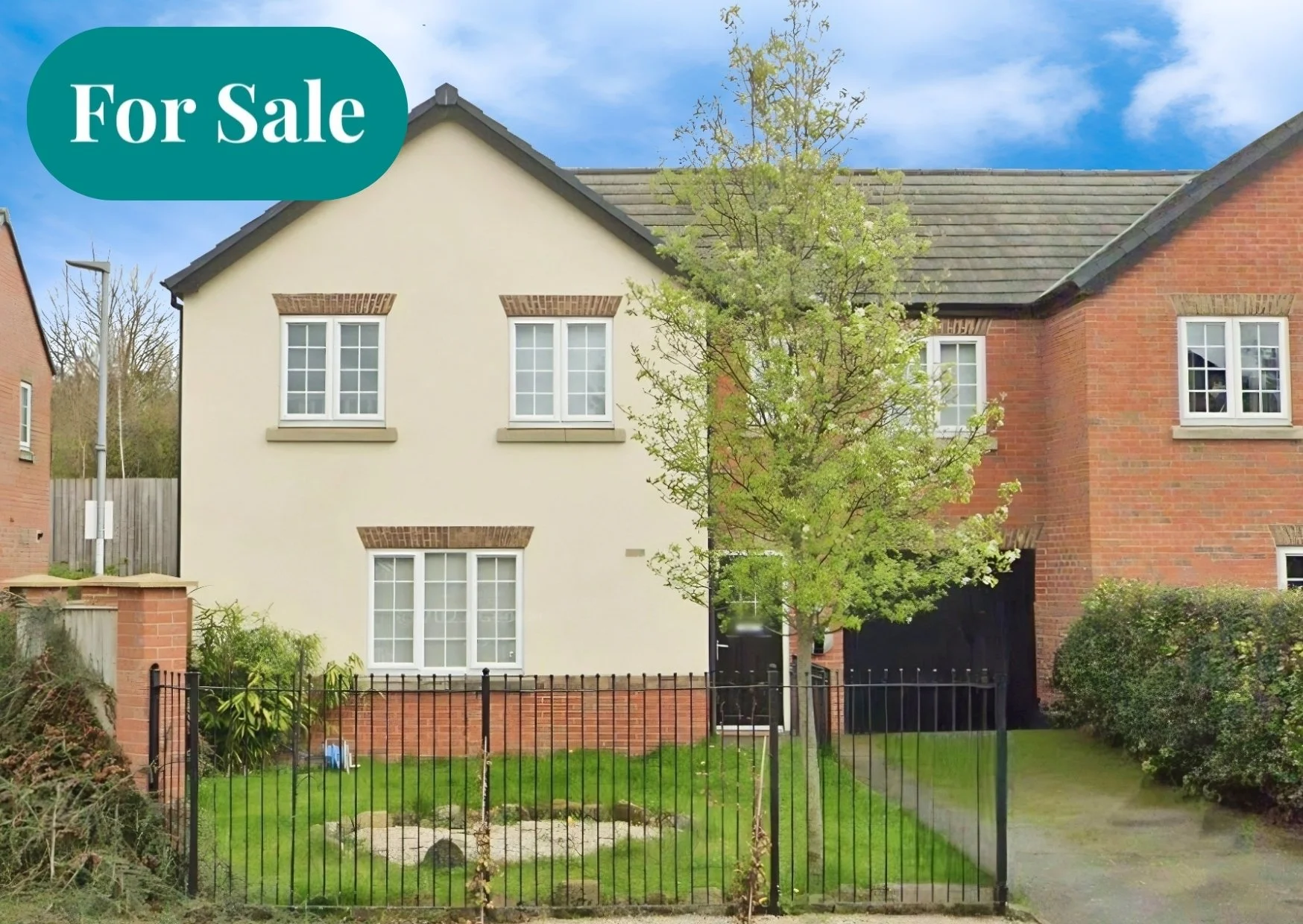 Photo of a house with a cream-colored facade and brick accents, surrounded by a small fenced yard, with a tree in front and a blue sky overhead. A