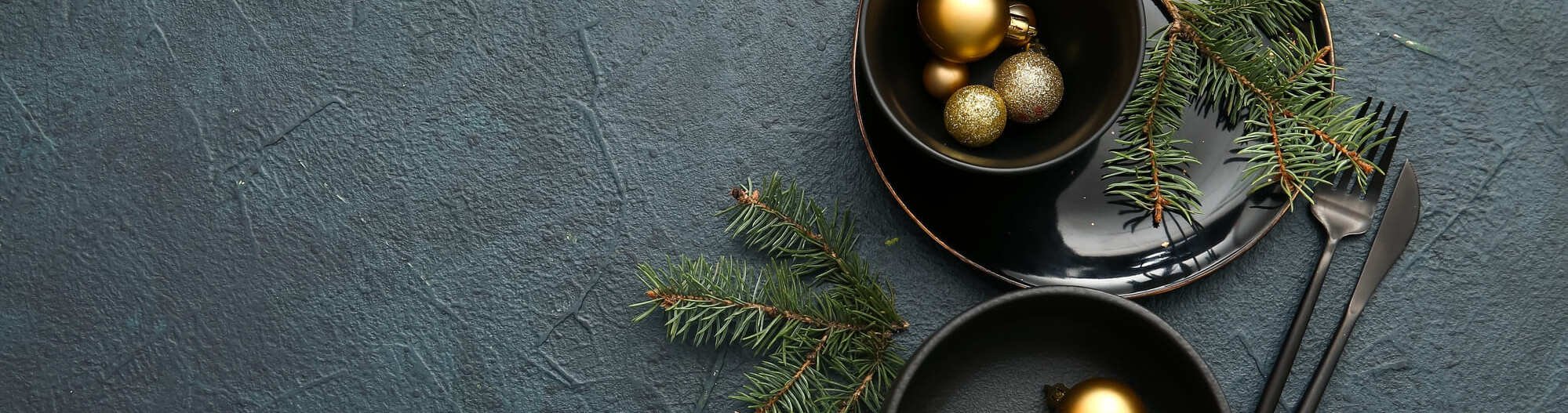 A sophisticated Christmas table setting with dark ceramic plates, gold baubles and fir twigs