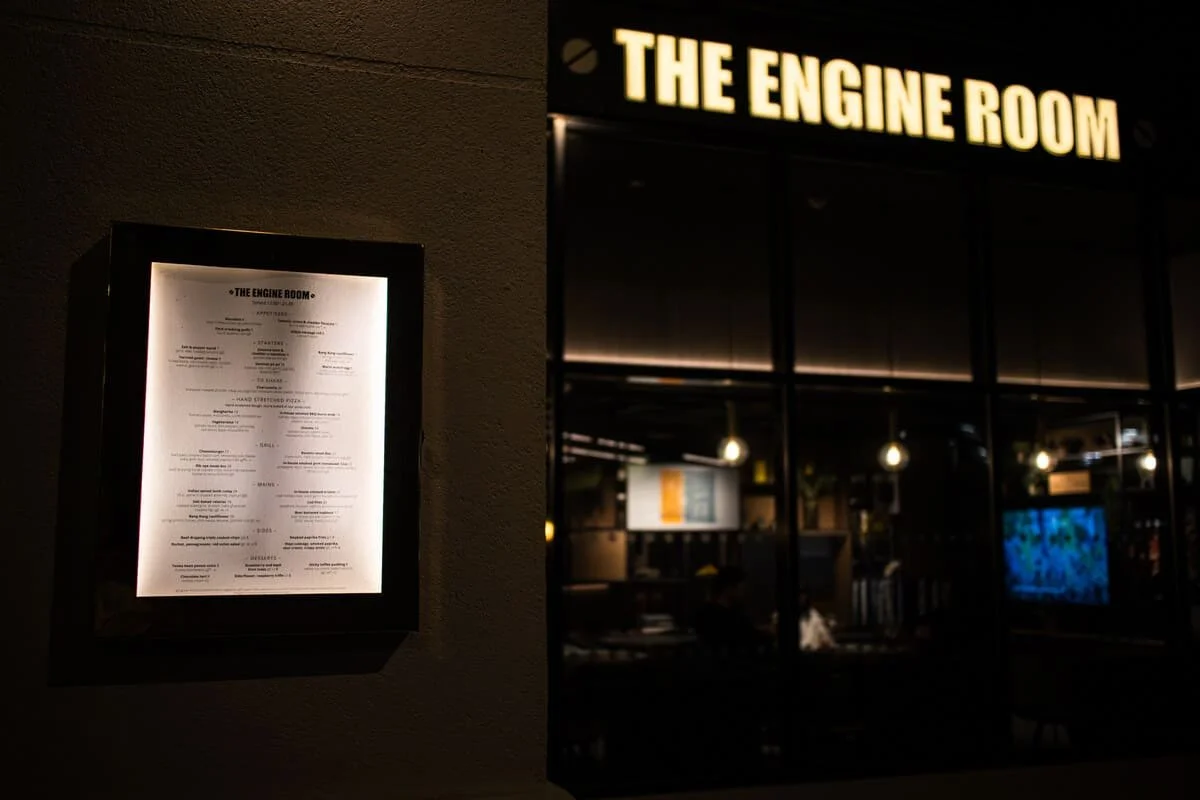 A lit directory or menu case for The Engine Room restaurant and a window showing the interior with hanging lights.