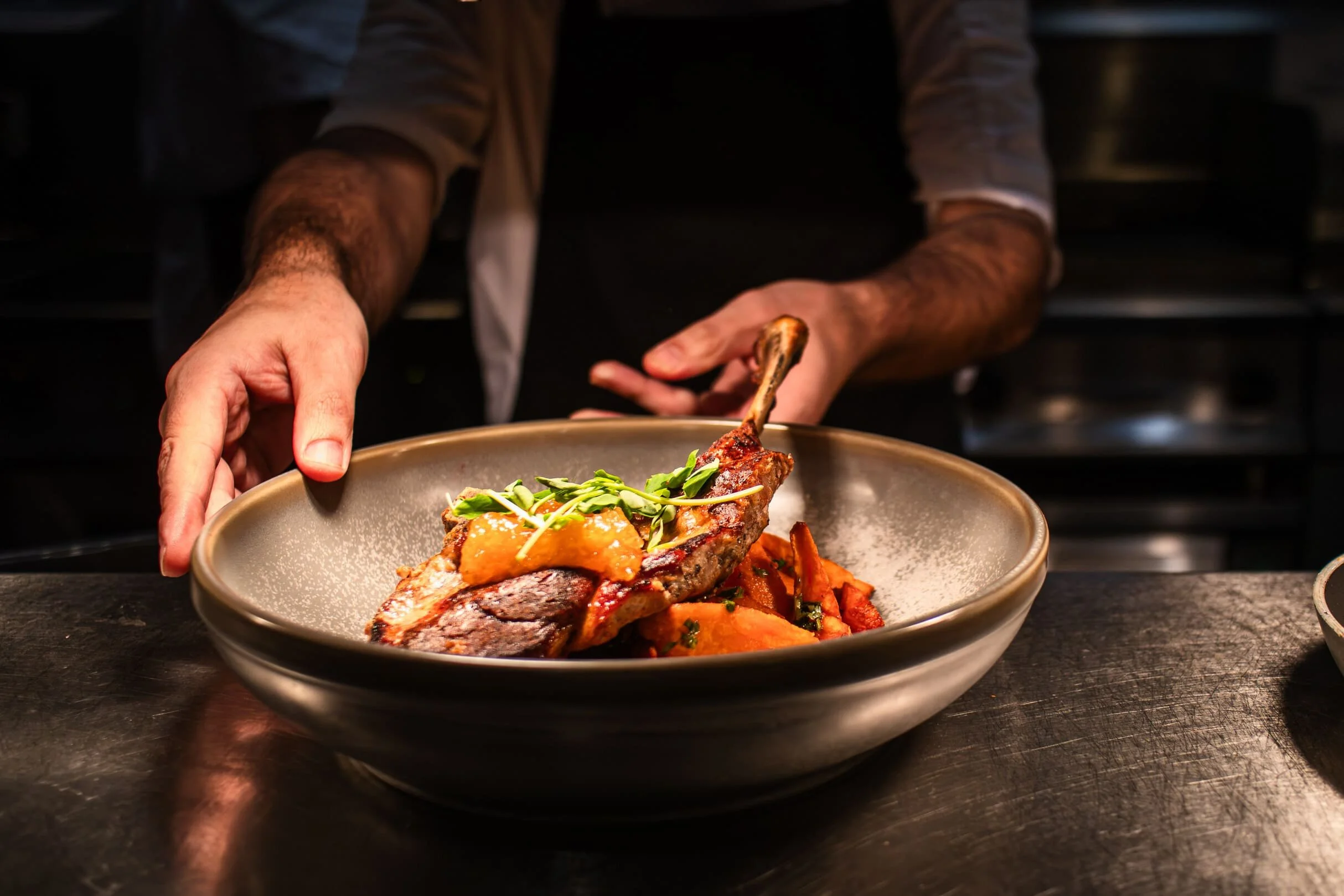 Close-up of a chef passing the in-house smoked pork tomahawk through the pass at The Engine Room.