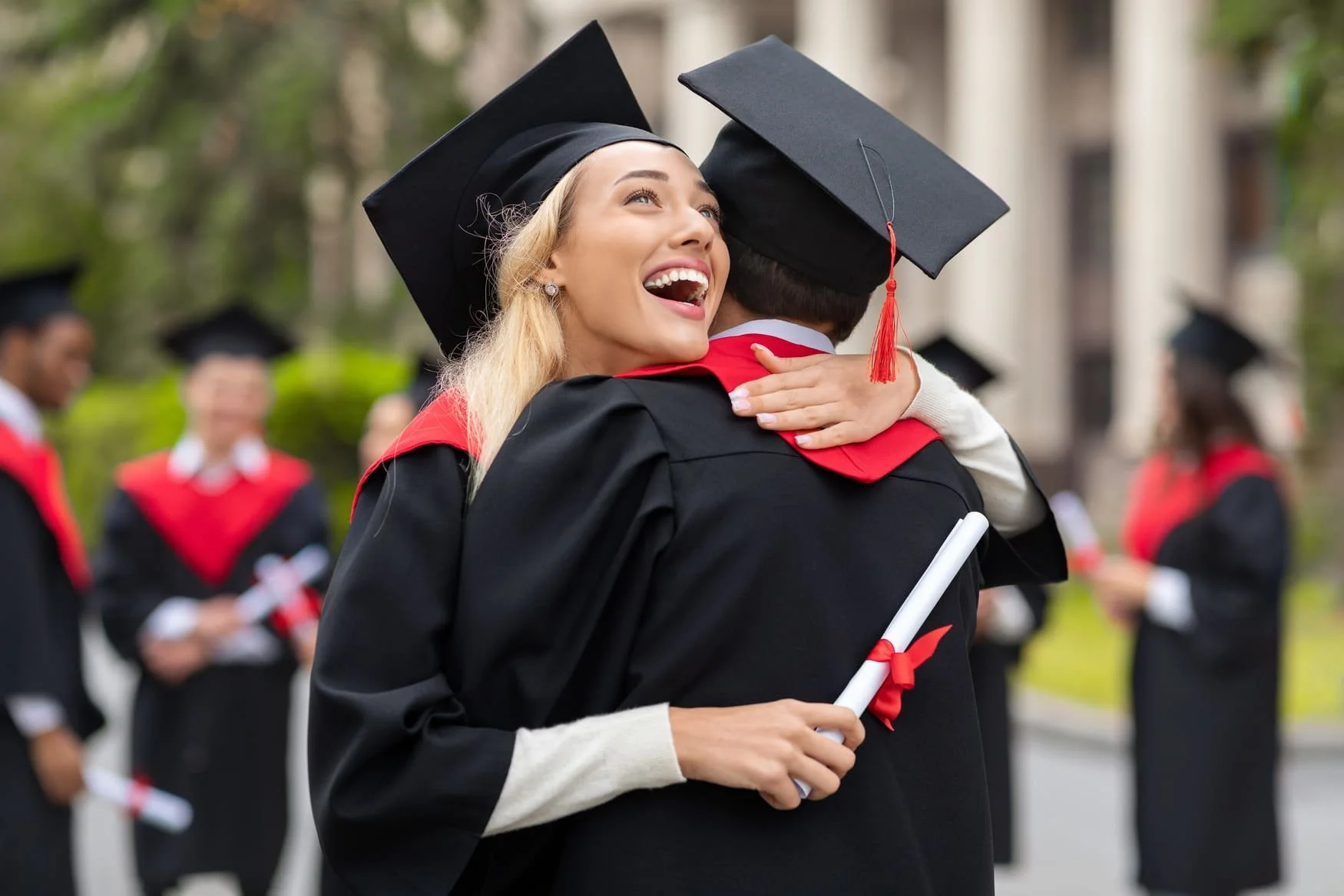 Two delighted graduates in caps and gowns hug