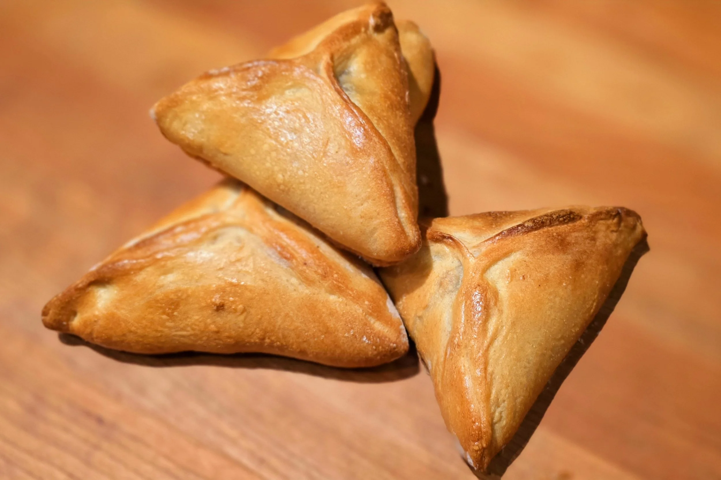 Three crispy, golden samosas on a wooden surface.