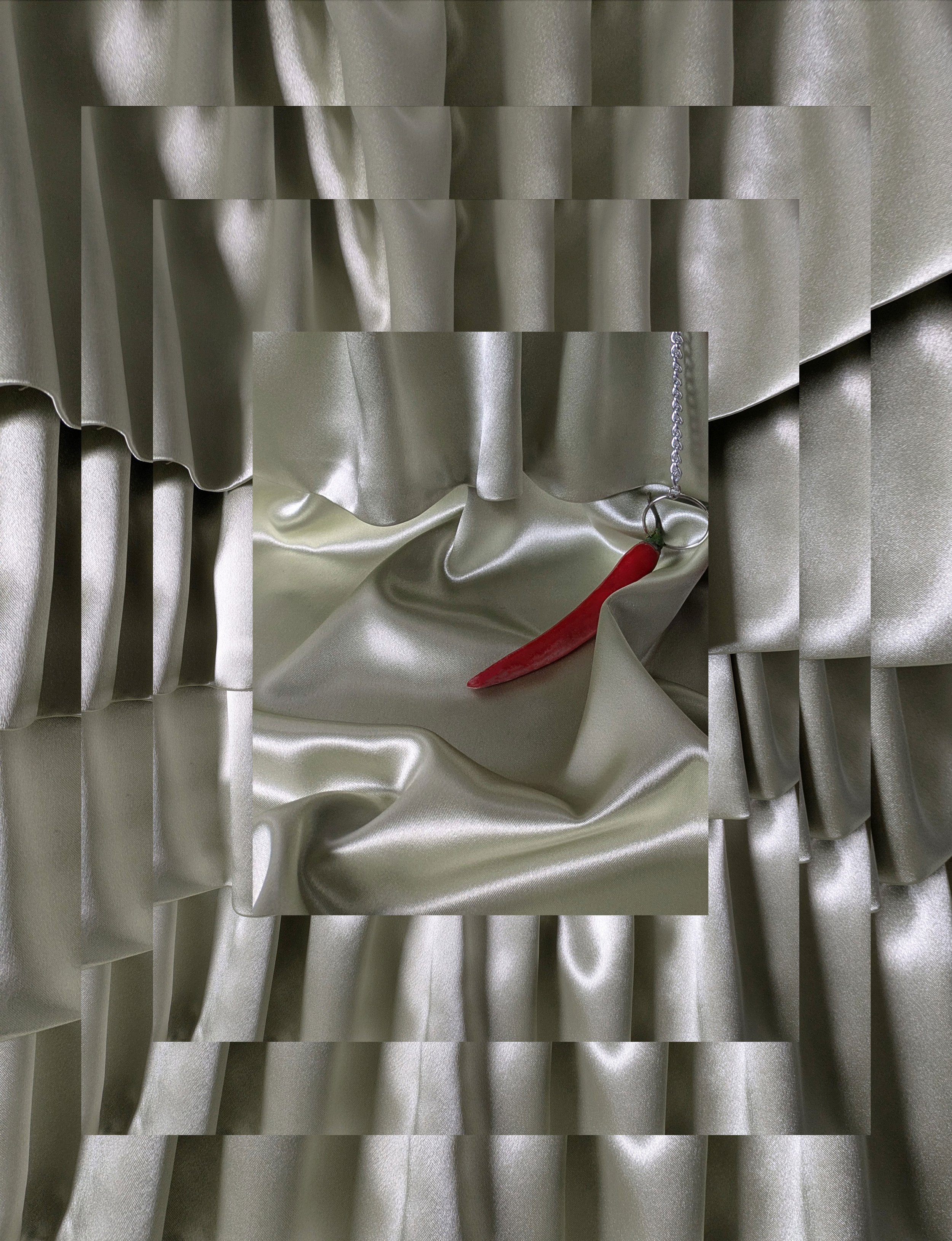 A digital collage with satin fabric in silver tones and a red chili pepper on a chain as the focal point.