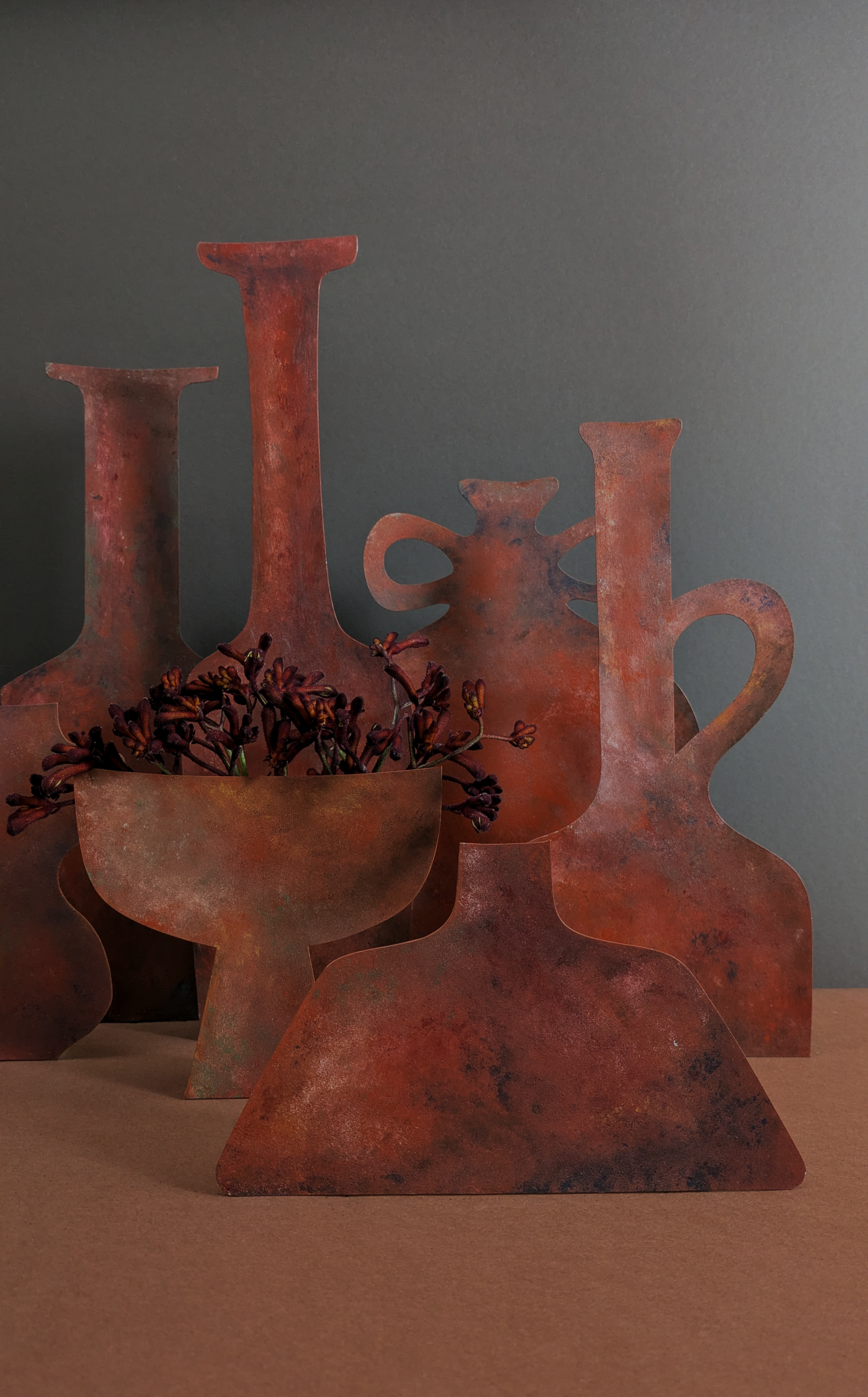 Decorative copper vessels and a bowl with dried purple flowers on a wooden surface.