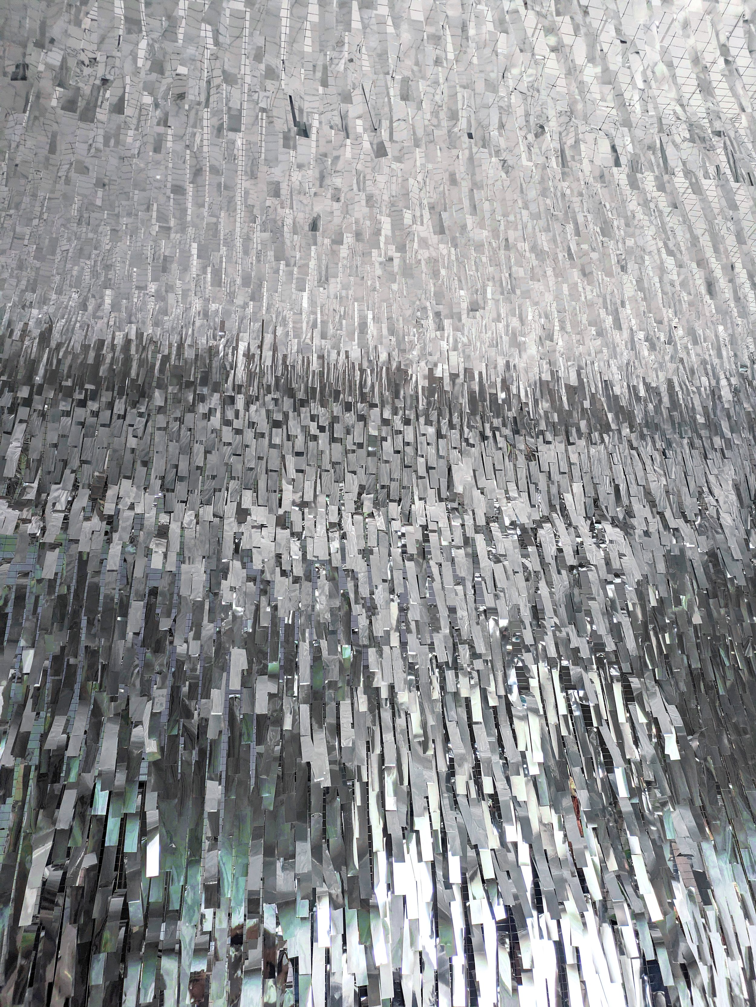 Close-up of a mirrored, textured surface consisting of small, rectangular, reflective tiles arranged in a flowing, wave-like pattern.