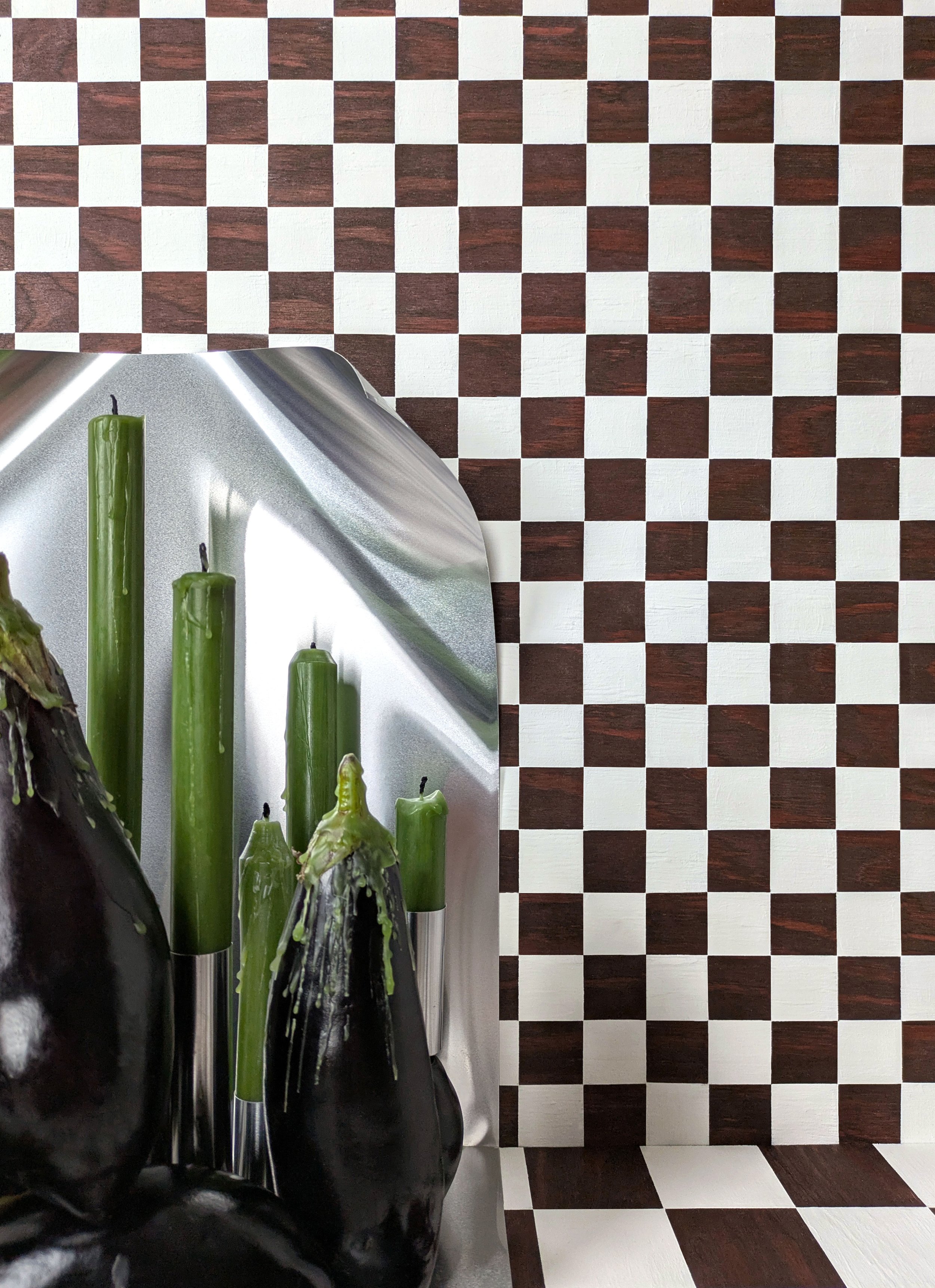 Black eggplants and green candles on a kitchen counter with a checkered brown and white wall.