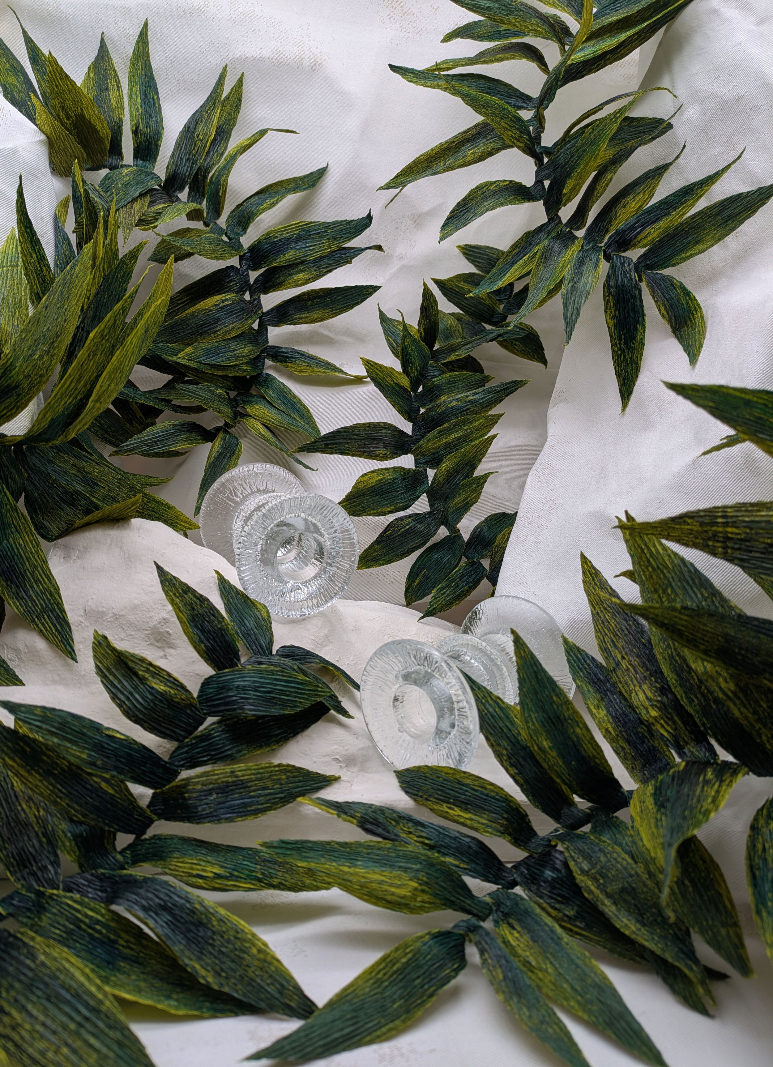 Green and black variegated leaves arranged around three clear glass circular objects on white fabric.