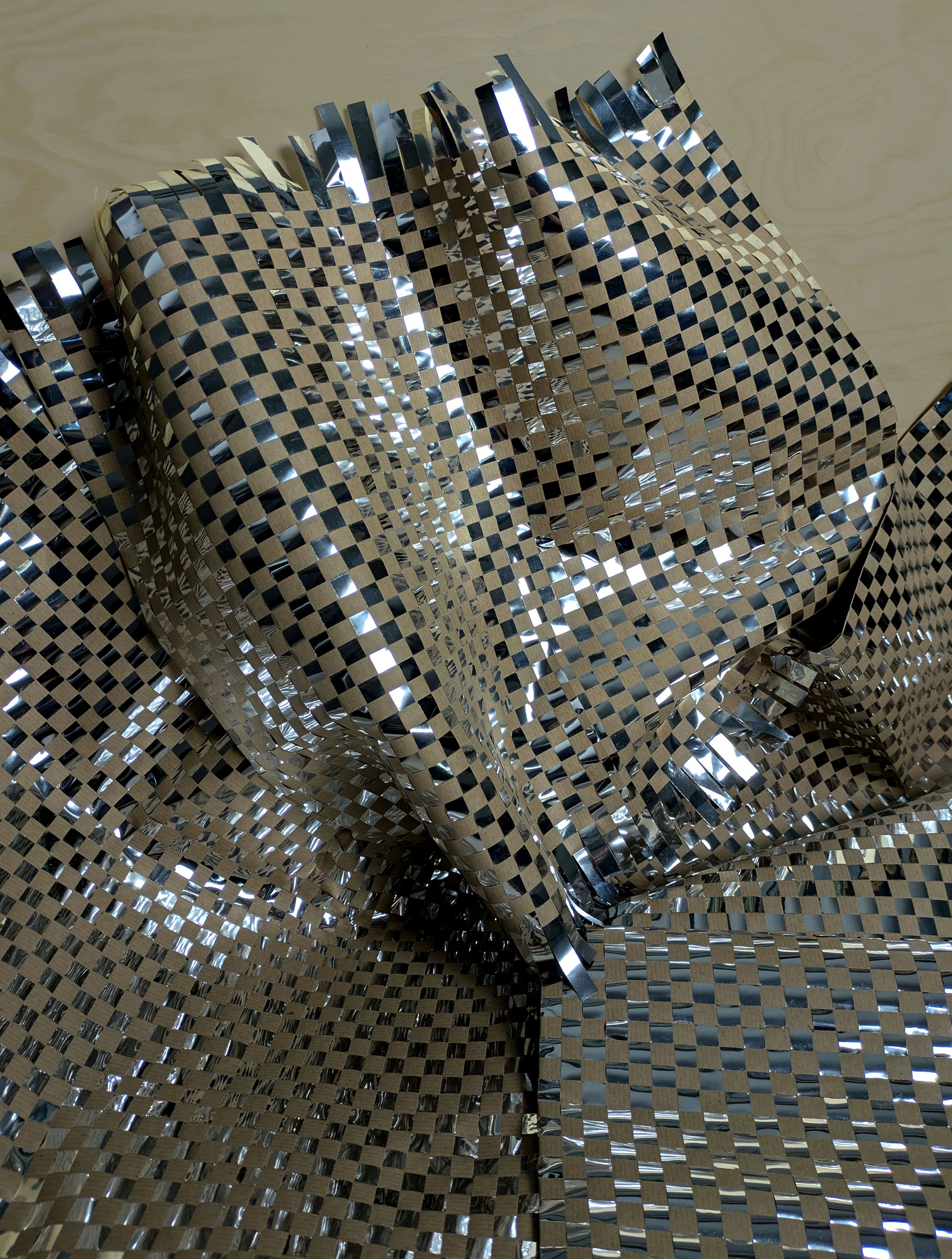 Reflective metallic foil with a checkered pattern, crumpled and layered against a beige background.