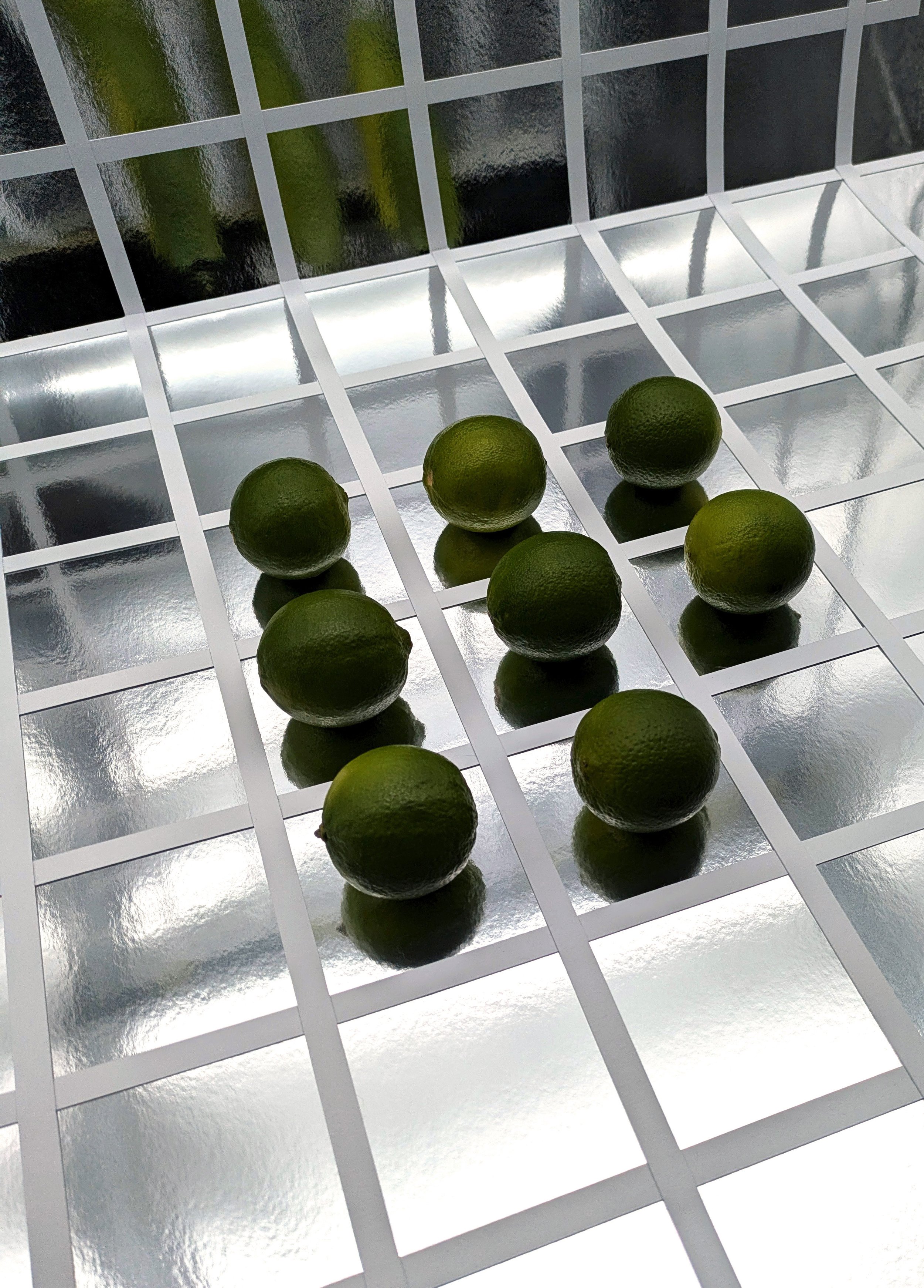 Seven limes arranged on a reflective metallic grid surface with a mirrored background.
