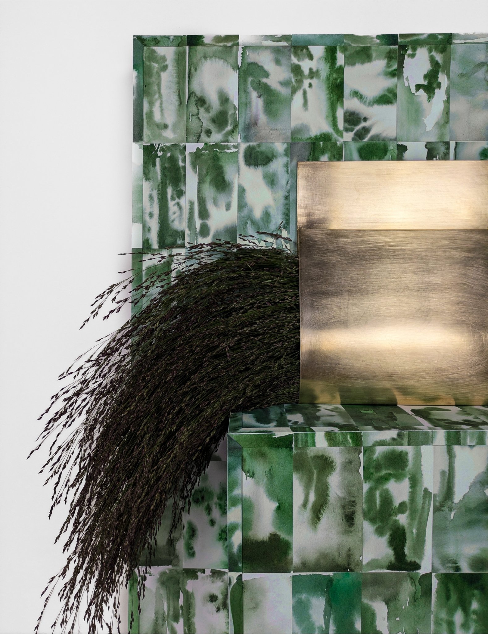 Interior decor featuring a green and white abstract tile wall, a textured metallic gold partition, and a bunch of dark purple ornamental grass.