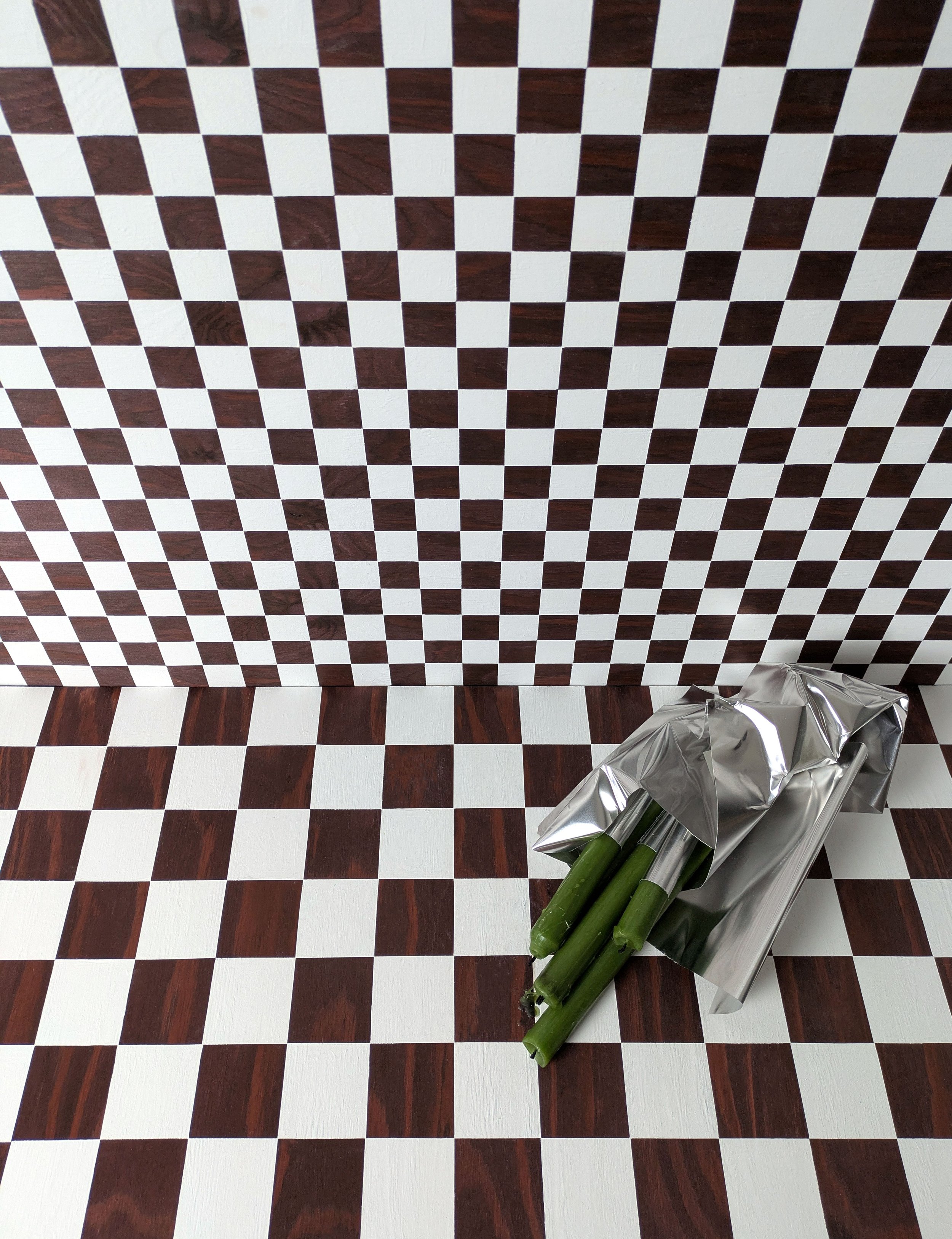 A room with black and white checkered walls and flooring, and newspapers with green vegetables on top placed on the floor.