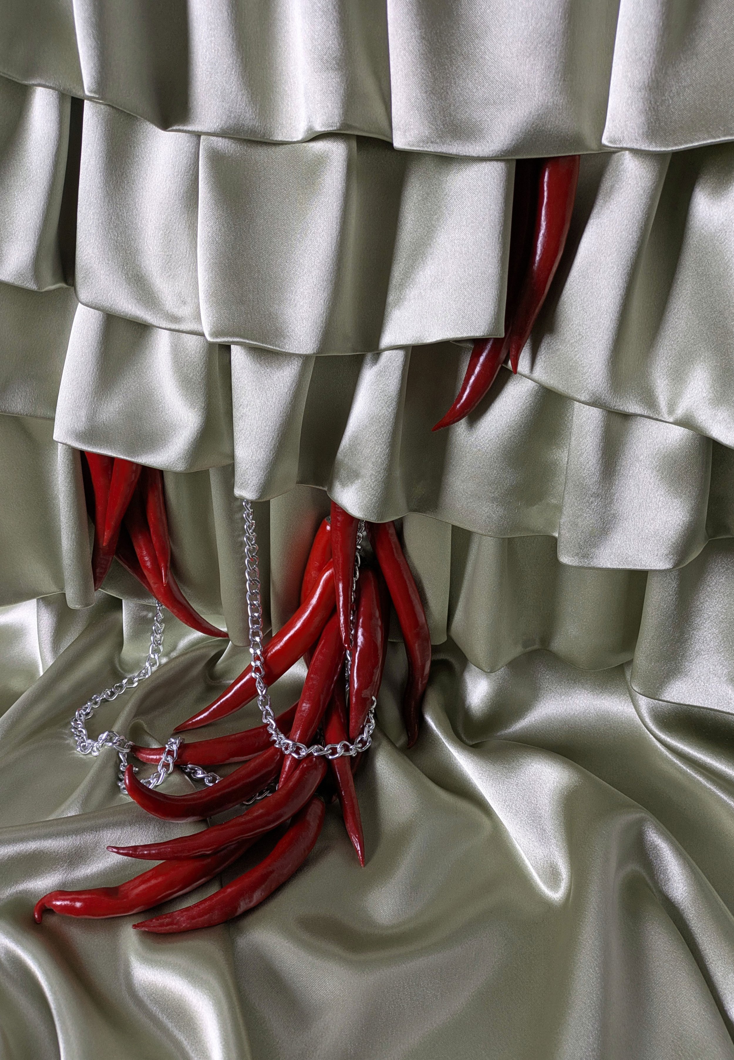 Red chili peppers with a silver chain resting on shiny gold satin fabric.
