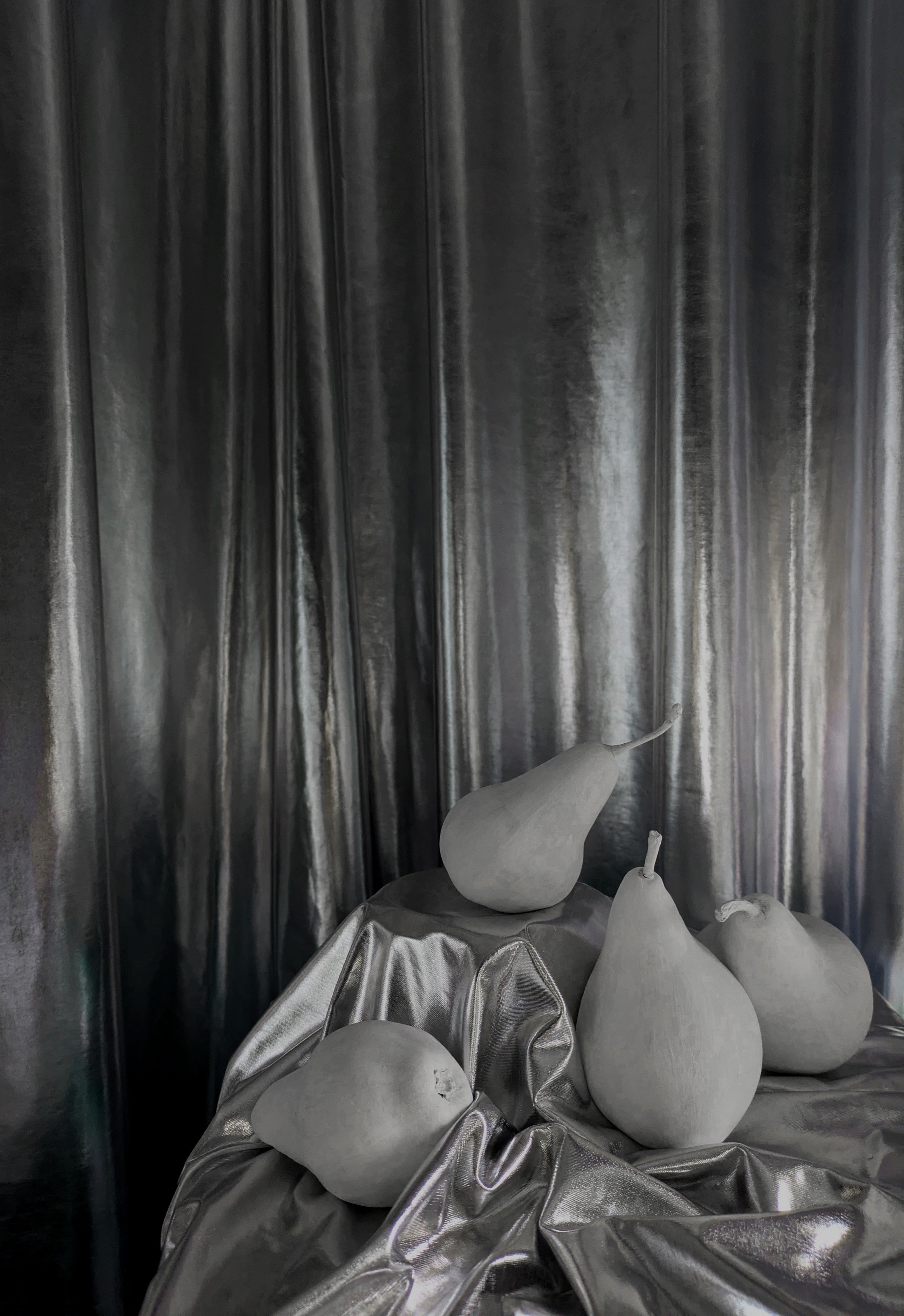 A still life arrangement of five pears on a shiny, draped surface with a reflective curtain backdrop.