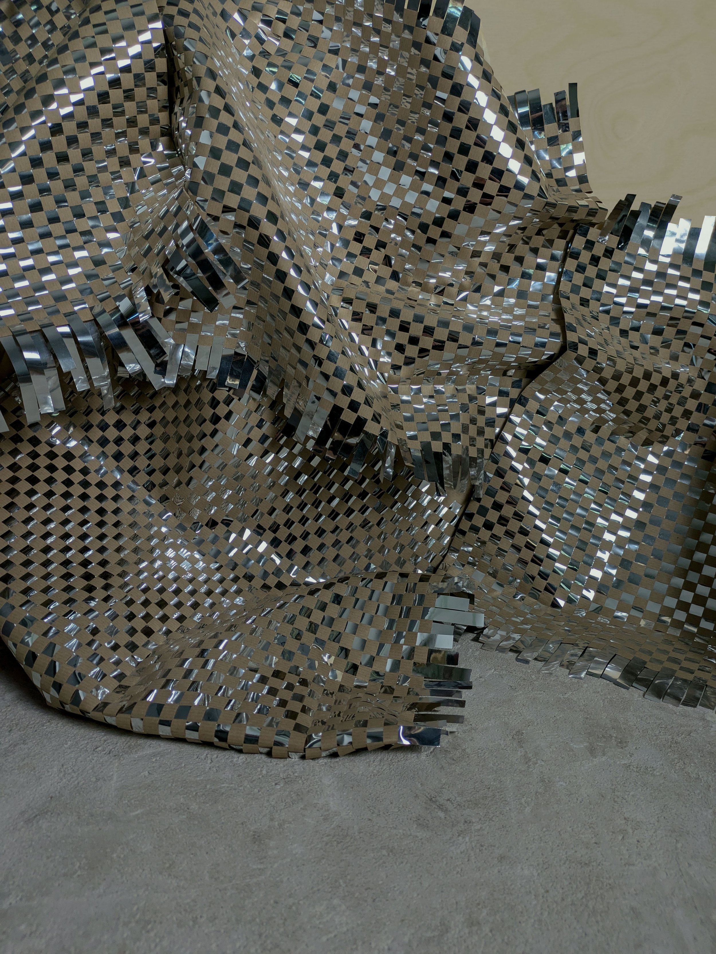 A crumpled sheet of reflective, checkerboard-patterned metallic material resting on a concrete floor.