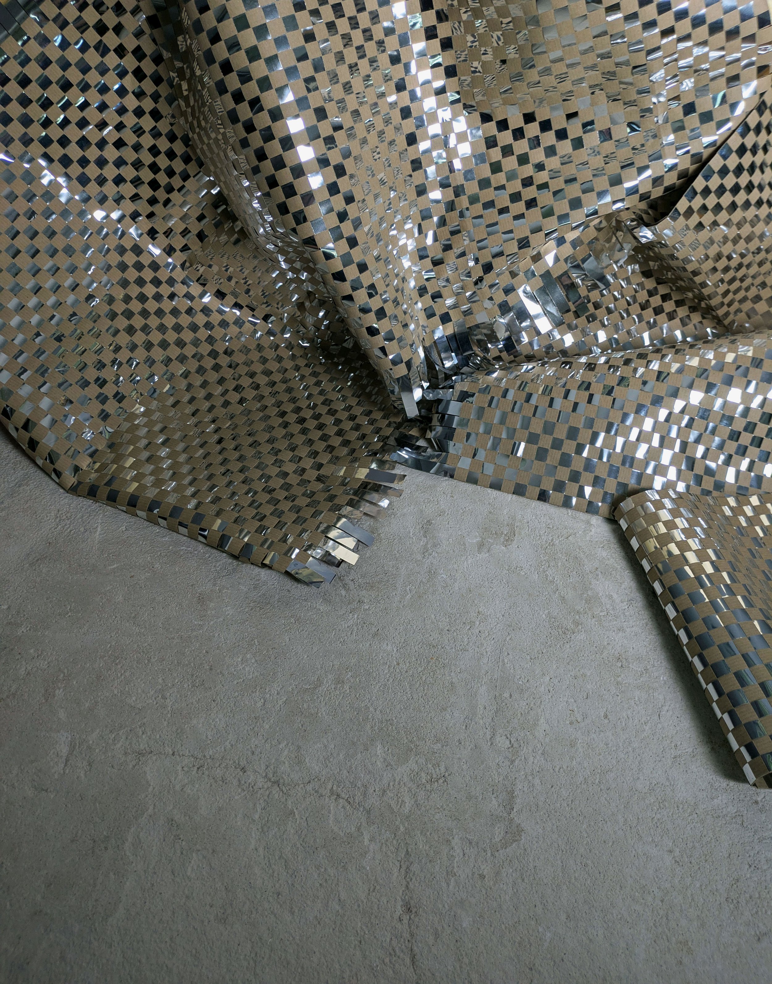 Close-up of crumpled metallic, reflective, checkered patterned metallic foil on a concrete surface.