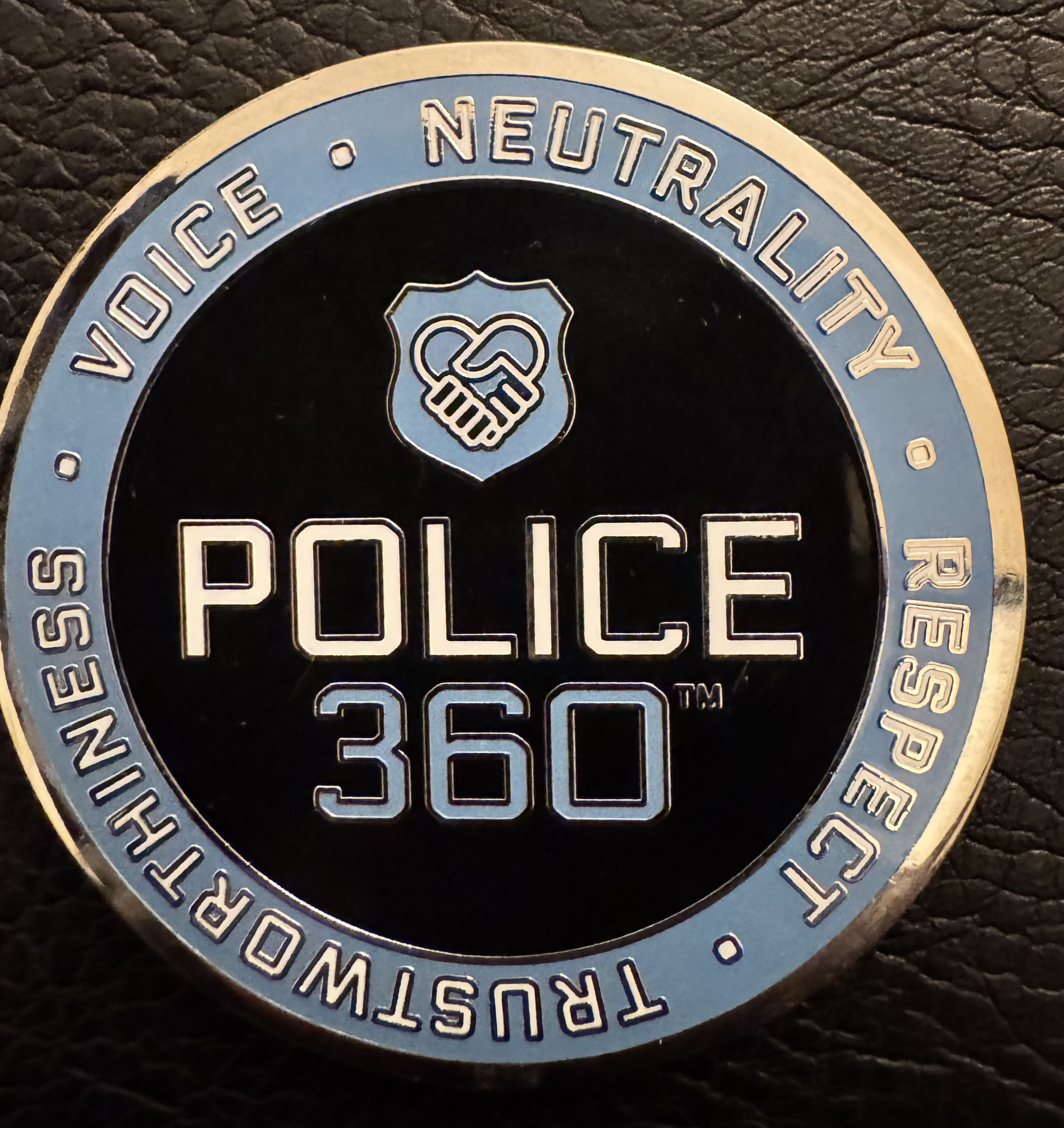 Close-up of a Police 360 Challenge Coin with the words "NEUTRALITY" and "POLICE" along with a shield emblem featuring two hands shaking.