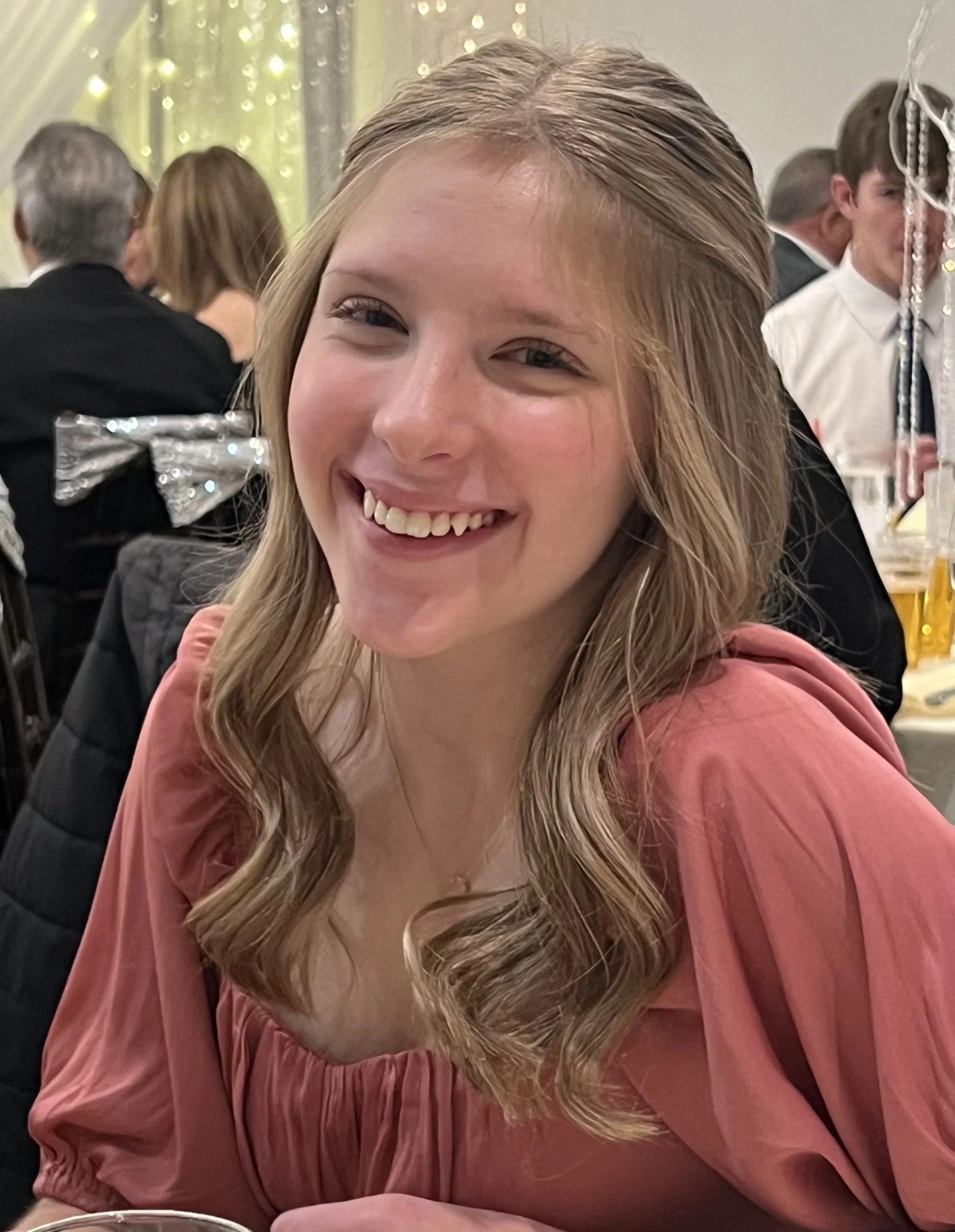 A young woman with wavy blonde hair smiling at a social event.