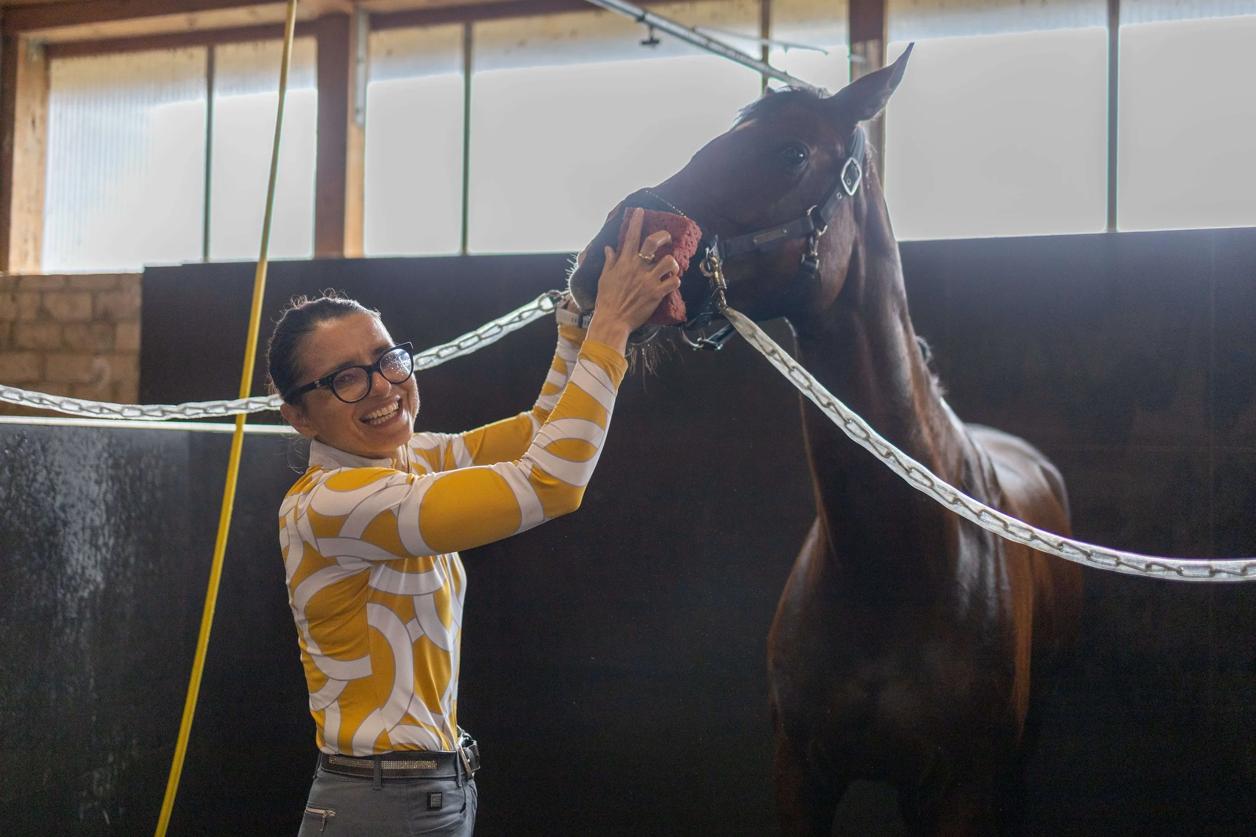 Woman gently interacting with a horse in a stable, captured with natural documentary photography.