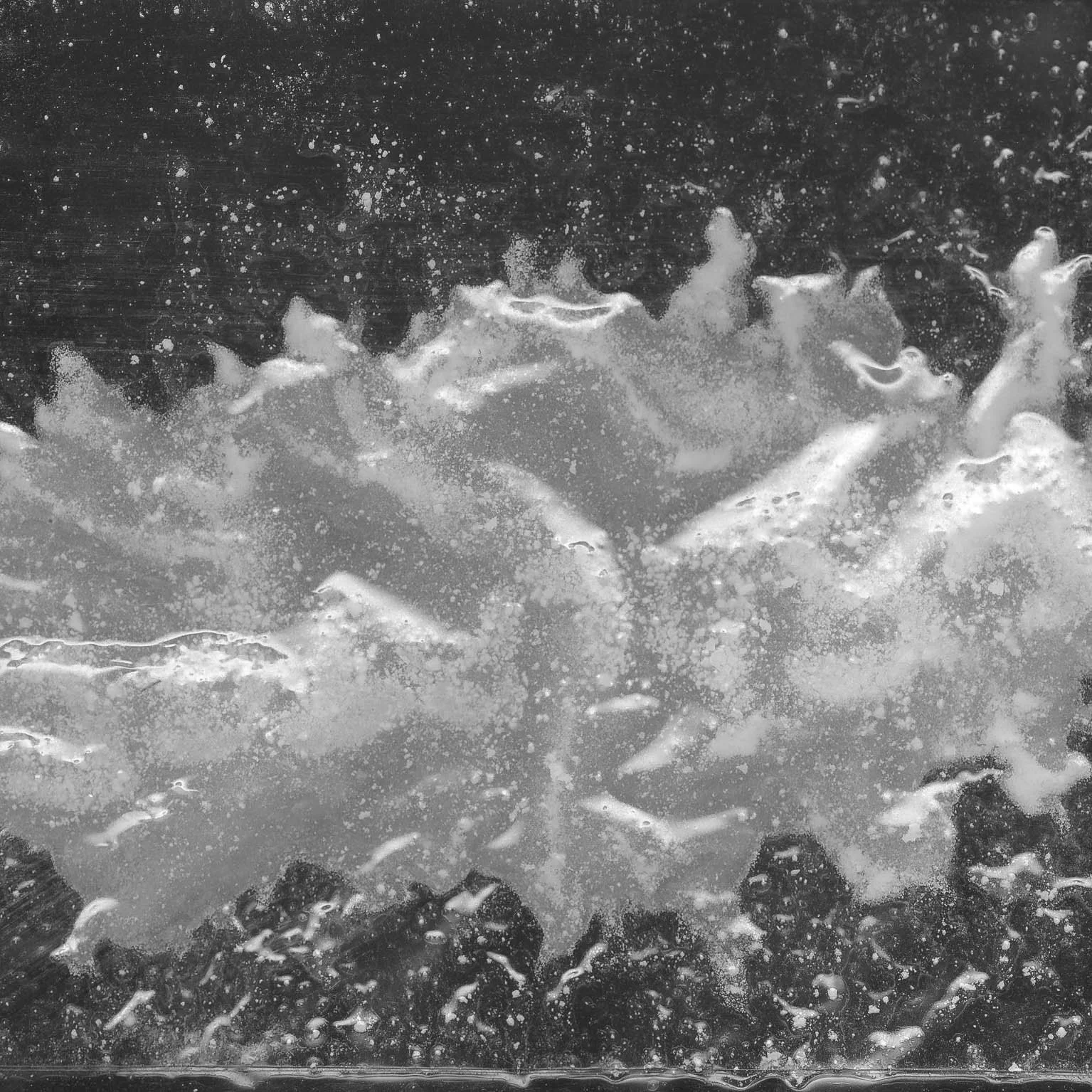 Close-up of soapy water with foam and bubbles on a surface, creating a textured pattern with reflections.