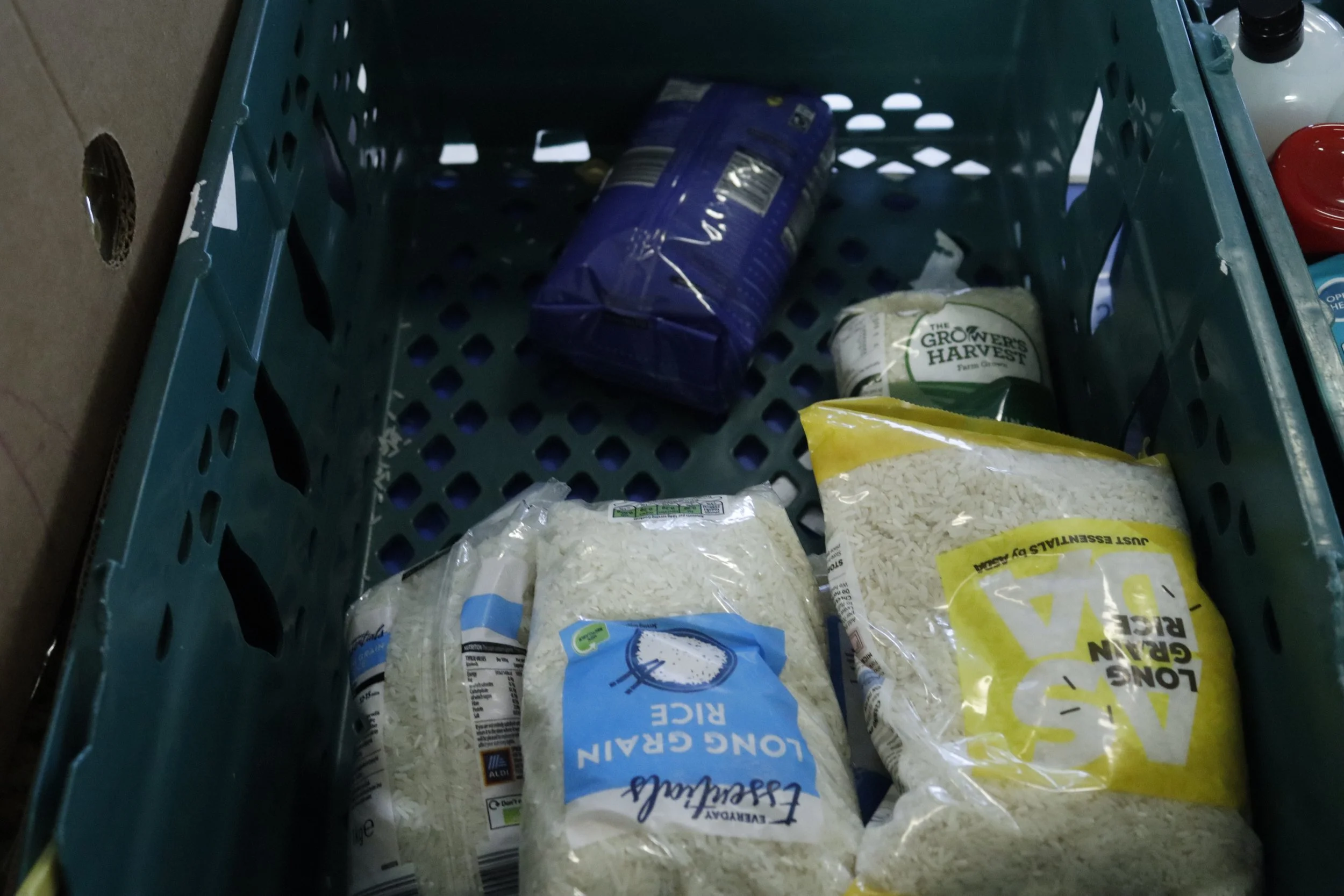 A green crate containing various packages of rice, including long grain rice and other brands.