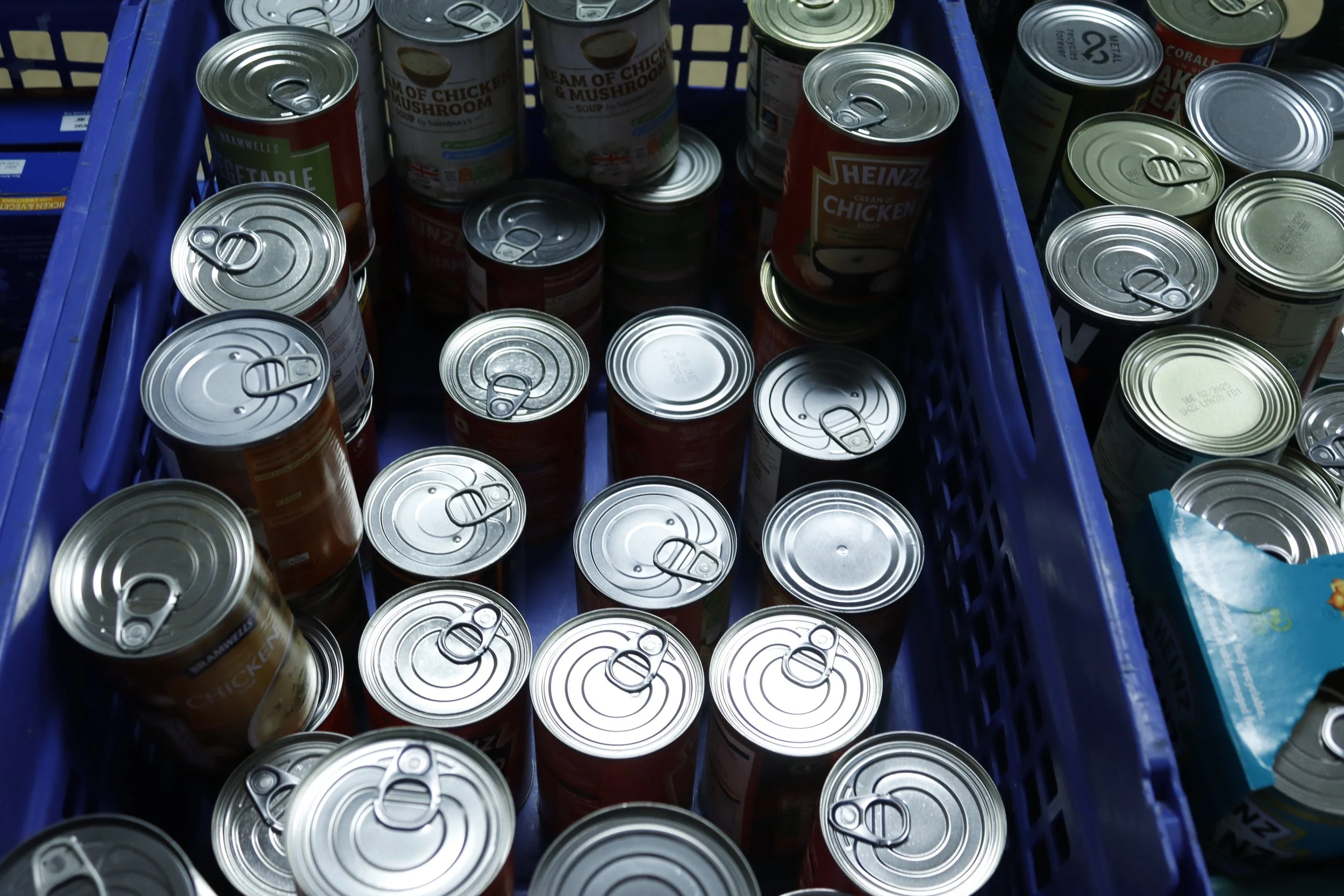 Assorted canned food in blue plastic crates, containing soups and beans.