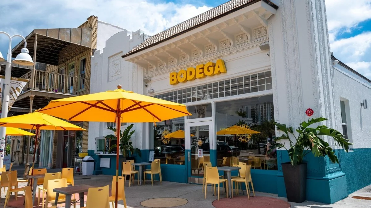 Exterior of Bodega in St. Pete with bright yellow umbrellas, outdoor seating, and the restaurant’s bold yellow signage on a sunny day.