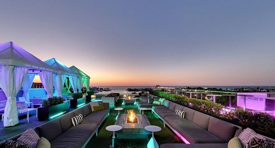 Rooftop seating at the Birchwood Canopy in St. Pete with glowing neon lights, firepits, and a sunset view over the water.