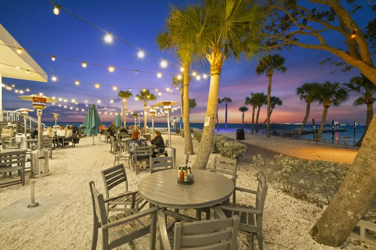 Nighttime waterfront dining at Doc Ford’s in St. Pete with string lights, palm trees, and a vibrant sunset over the bay.
