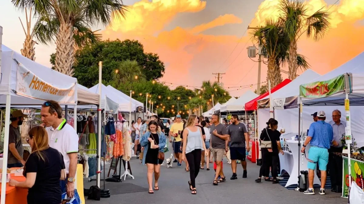 Crowds walking through the St. Pete Saturday Morning Market at golden hour with vendor tents, palm trees, and warm sunset colors in the sky.