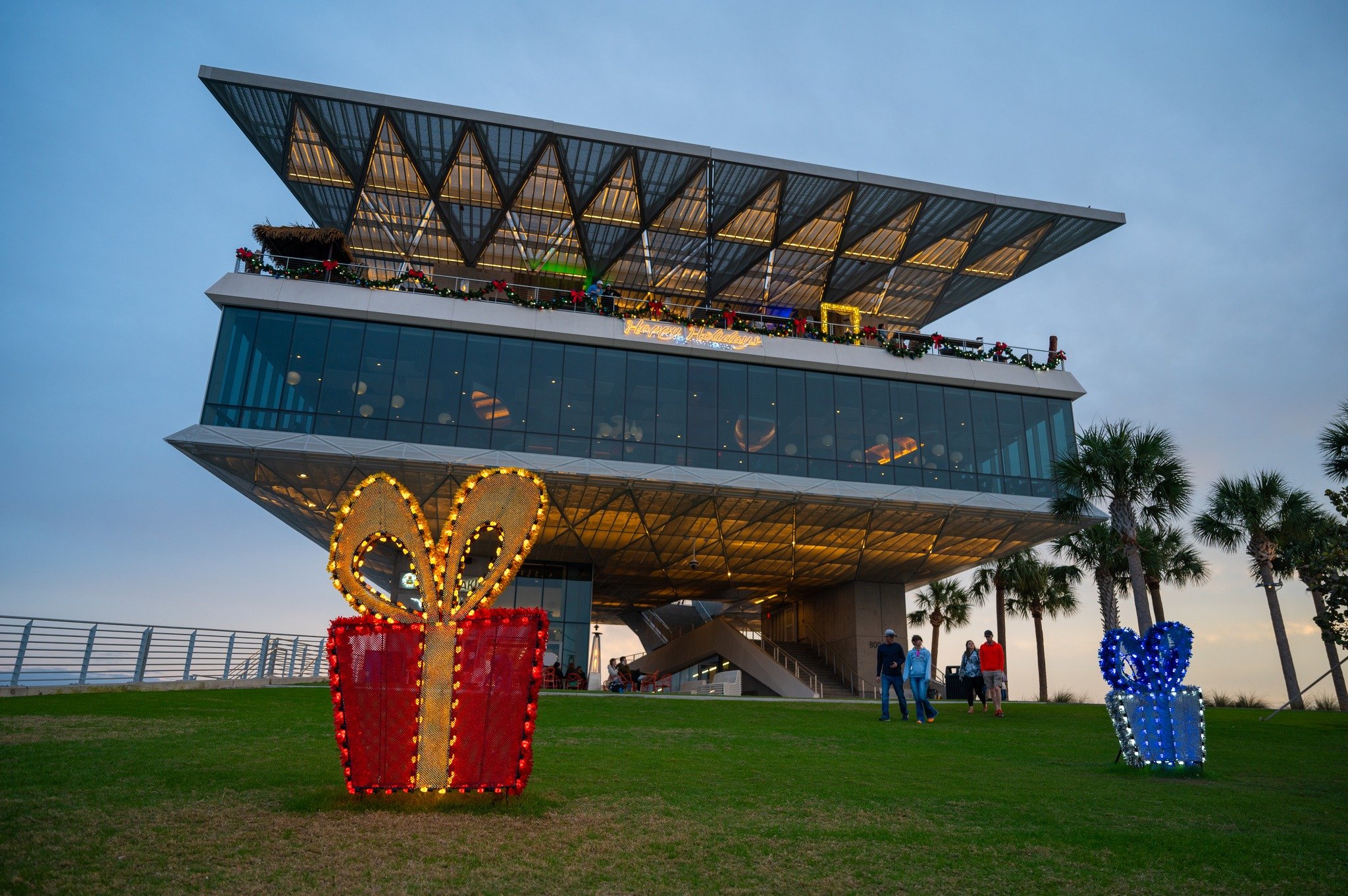 Holiday decorations at the St. Pete Pier featuring large illuminated gift displays and festive garlands on the building at dusk.