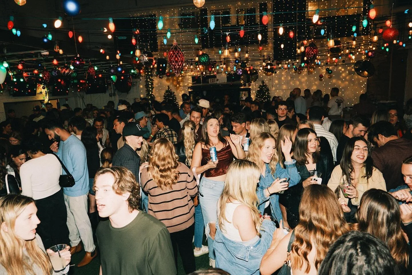 Crowded Christmas themed pop up bar in downtown St Pete with holiday lights, decorations, and people dancing and celebrating at night.